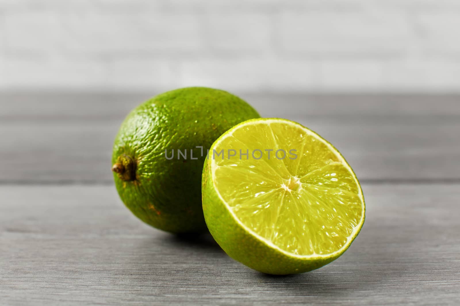 Whole lime and other one cut in half, on a gray wooden table.