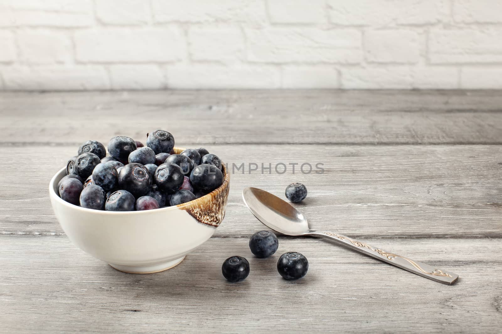 Small bowl of black blueberries with spoon next to it, placed on a gray wood table