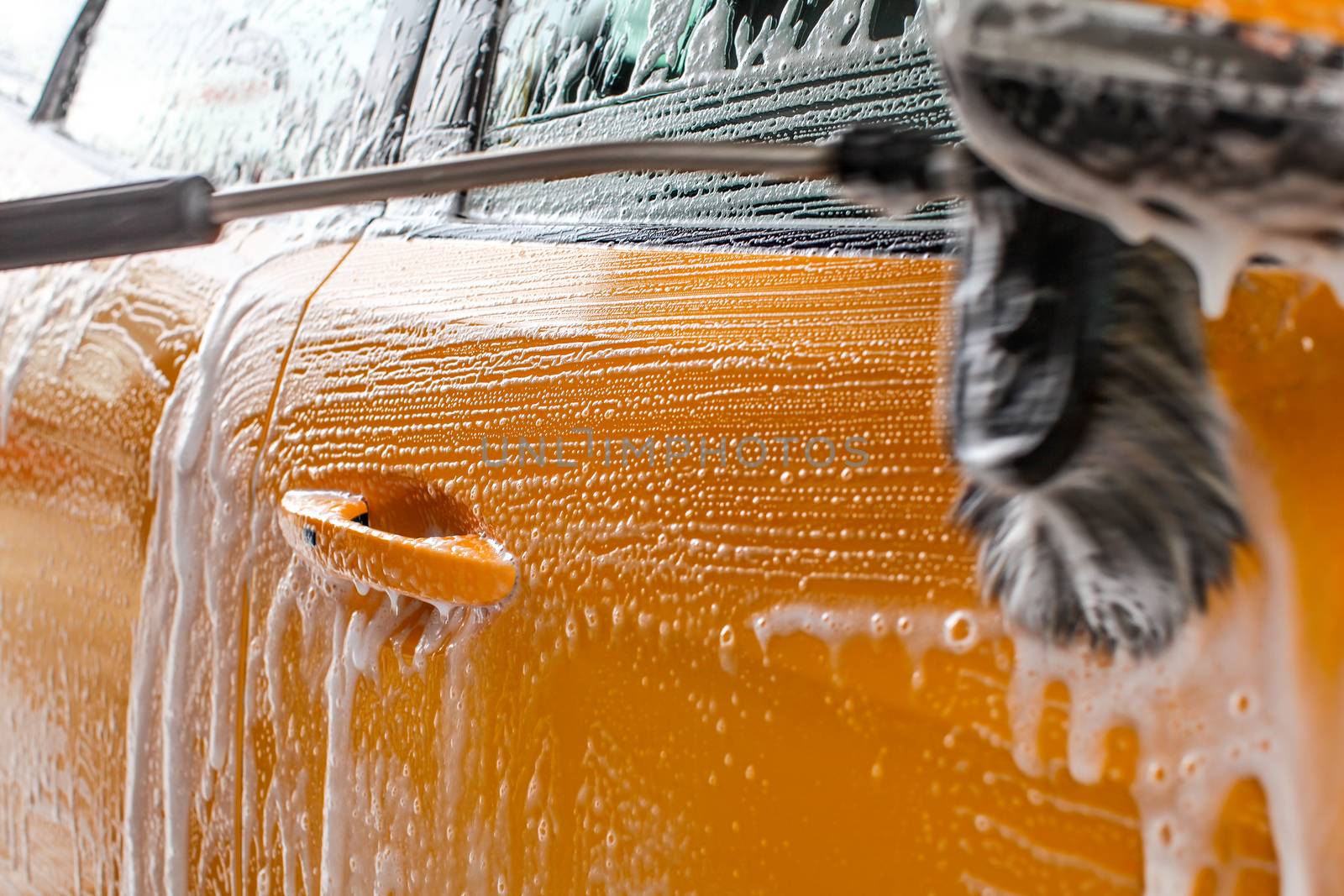 Detail of dark yellow car side washed in carwash. Brush leaving strokes in white soap and shampoo foam.