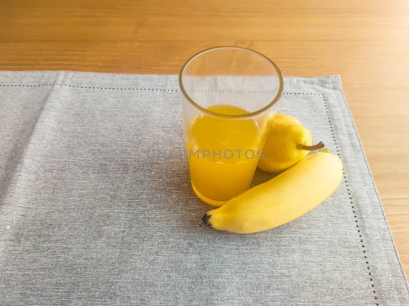 Banana, pear and glass of orange juice, on fabric towel, on the table and blurred background.