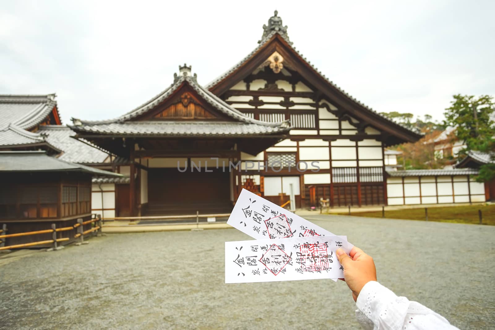 Kyoto, Japan - December 17, 2019 : Two tickets of Kinkakuji temple on Asian woman hand with Japanese style building background.
