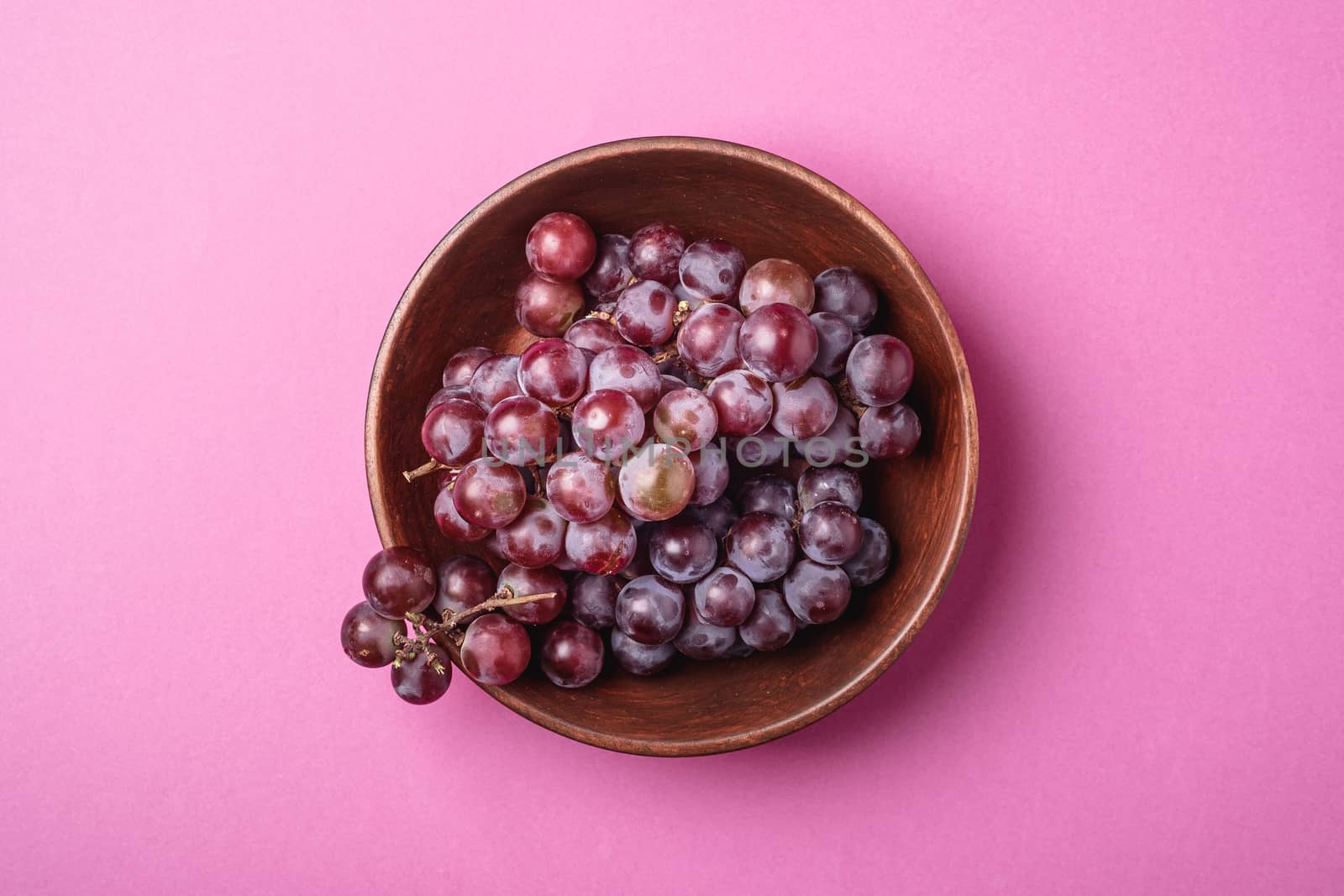 Fresh ripe grape berries in brown wooden bowl on pink minimal background, top view