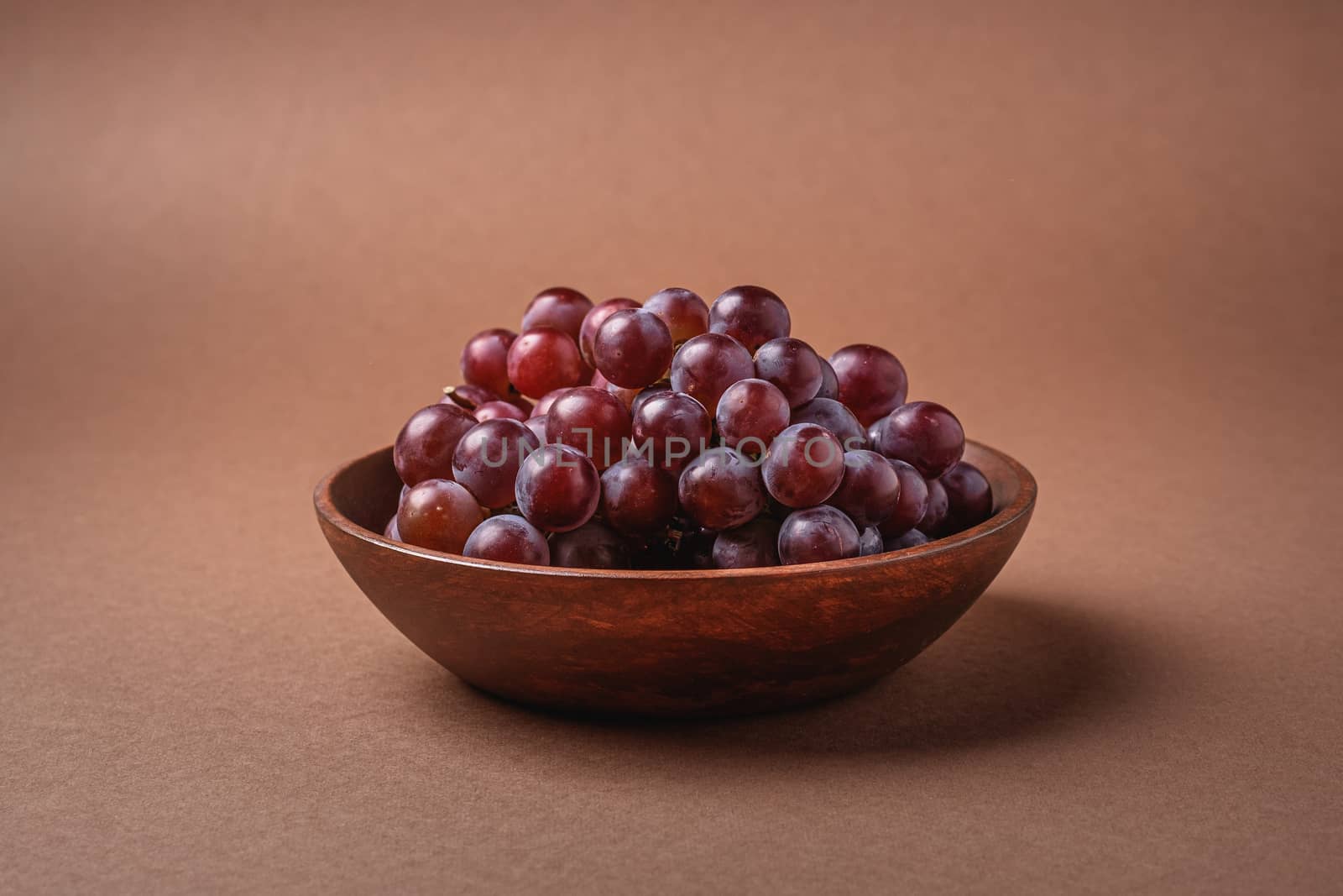Fresh ripe grape berries in brown wooden bowl on brown by Frostroomhead