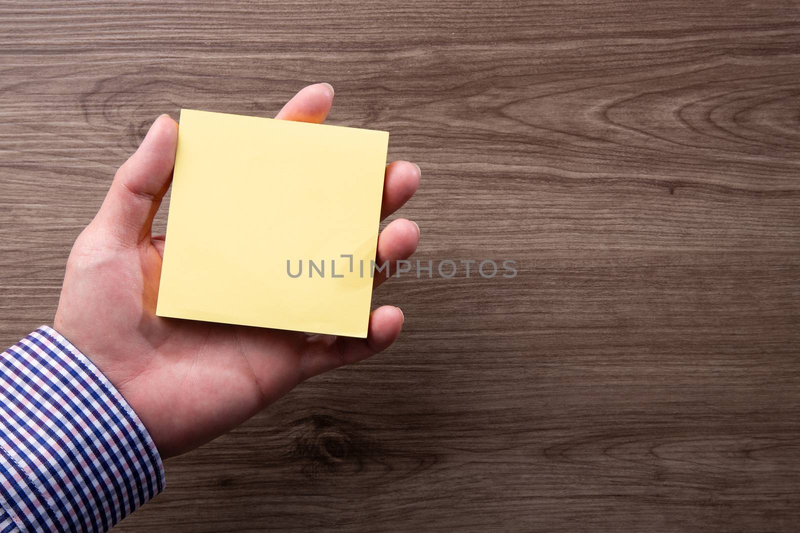 Hand holding sticky post note paper sheet on wooden background