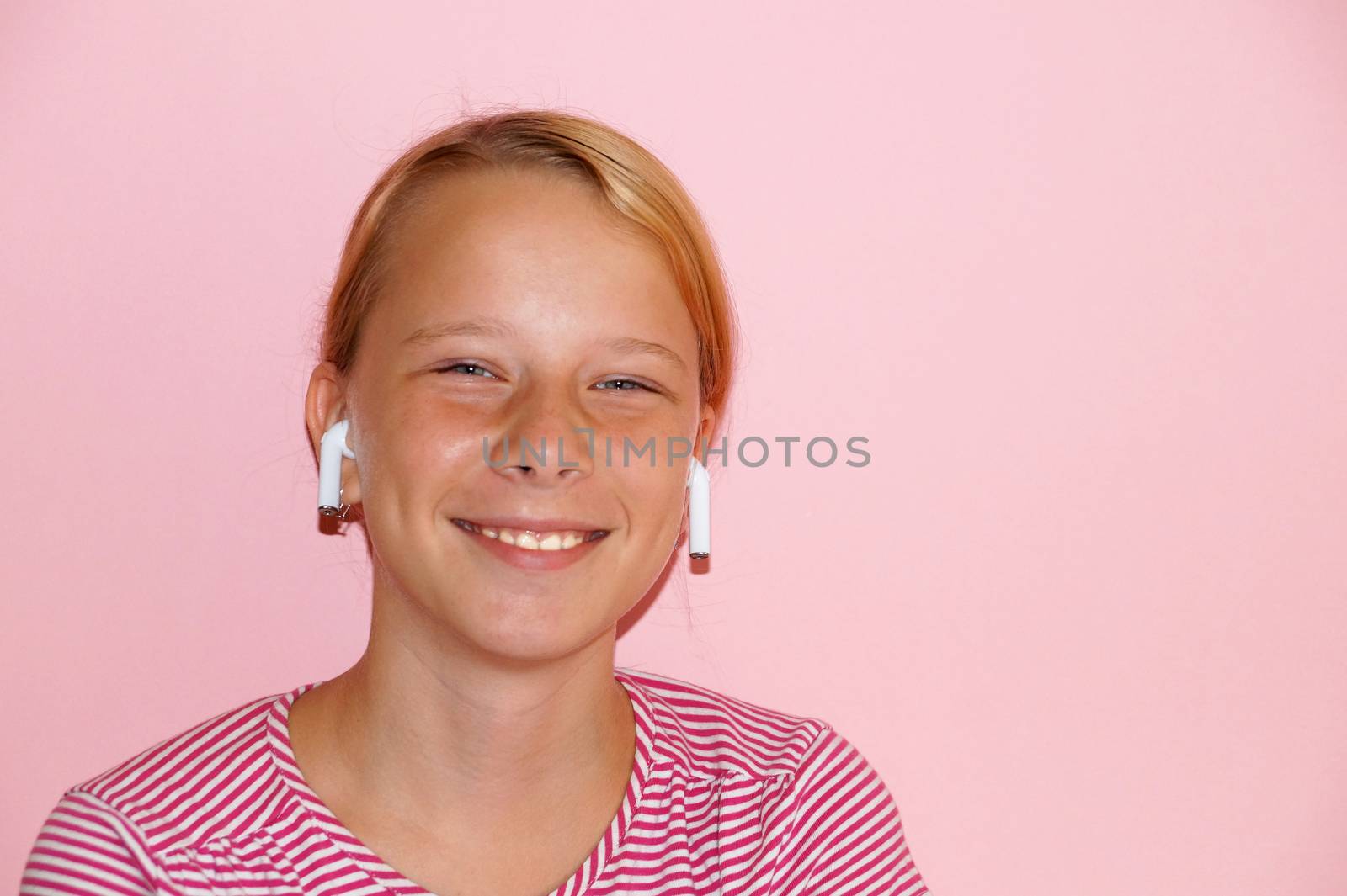 teenage girl listening to music on headphones and smiling, portrait on pink background by Annado