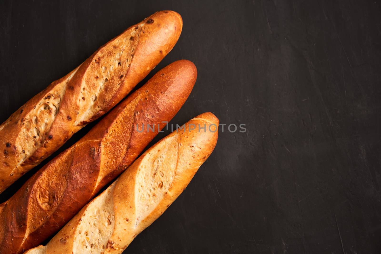 Three crispy french baguettes lie dark black table background sesame seeds Classic french national pastries Copy space Concept for menu or advertising