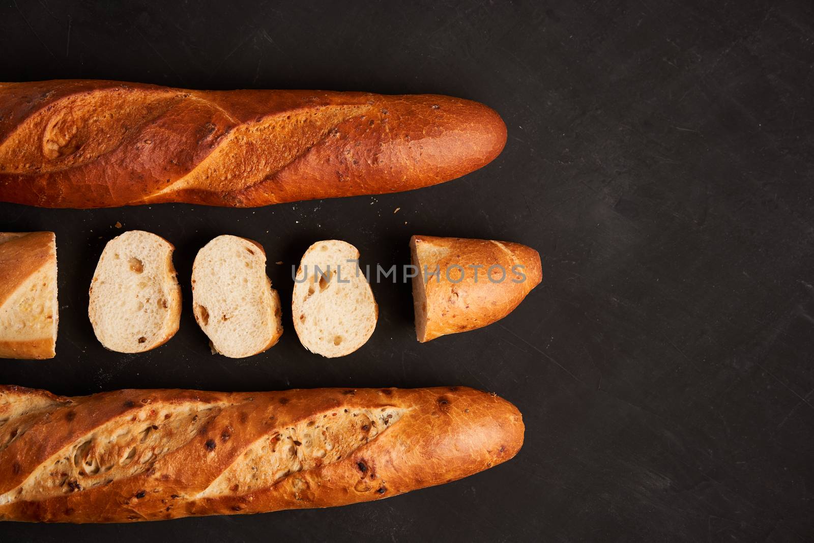Three sliced crispy french baguettes lie dark black table background sesame seeds Classic french national pastries Copy space Concept for menu or advertising