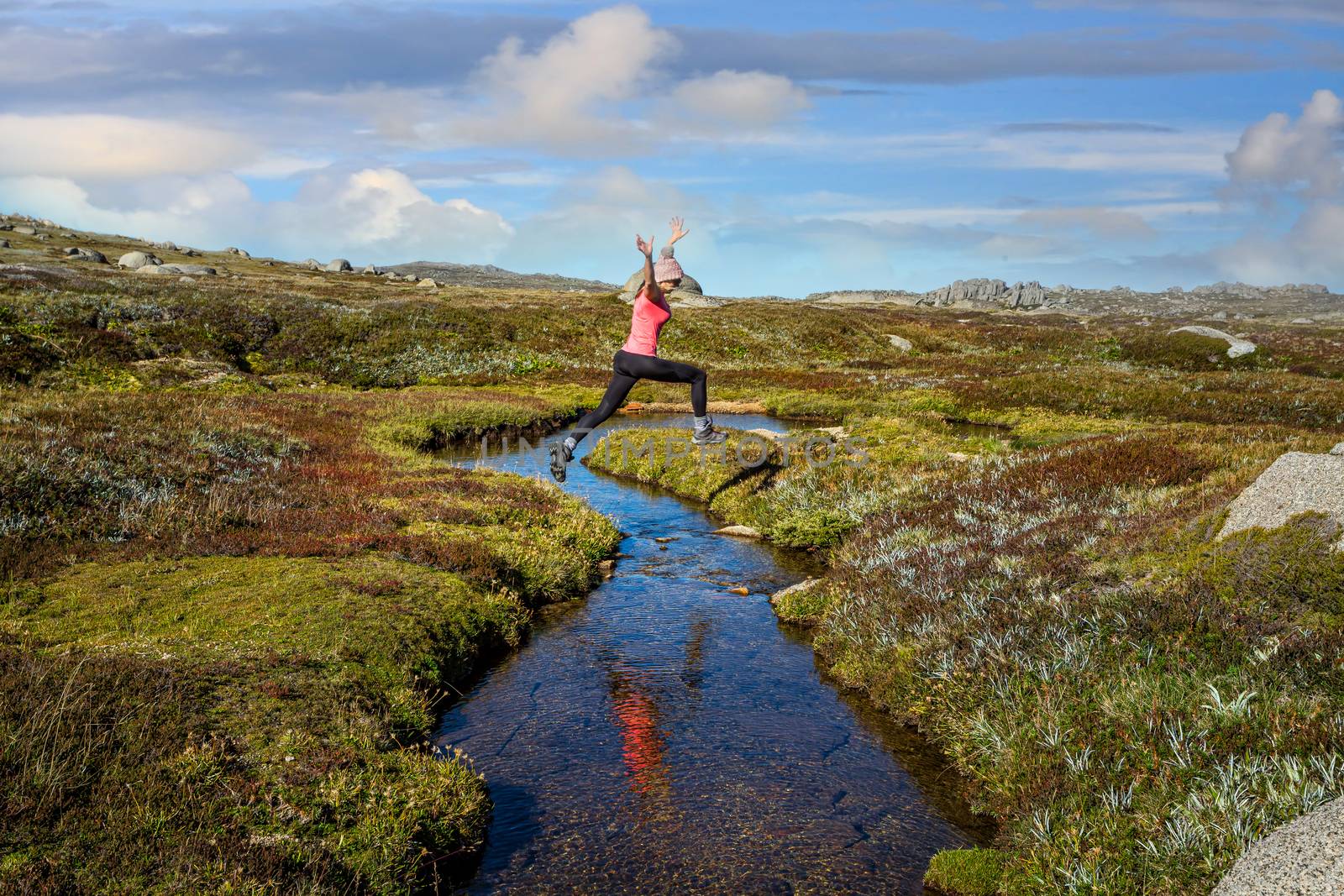 Woman run free jumping little meandering stream in high country of Australia