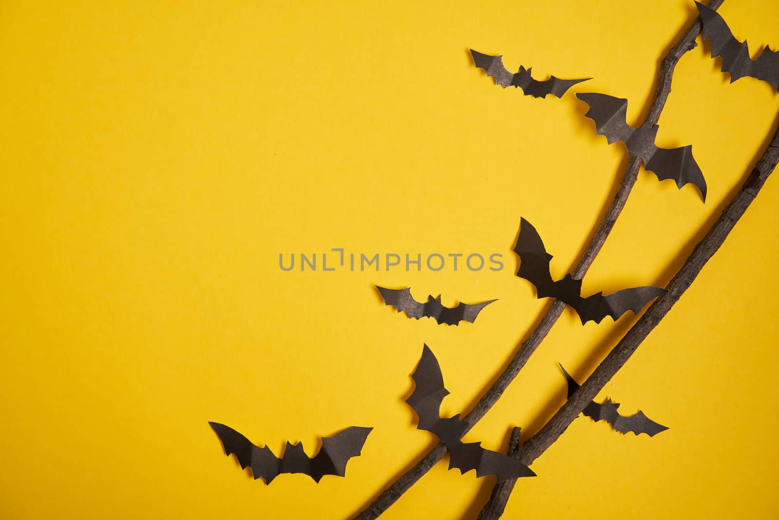 Halloween decoration concept black paper bats dry branch stick yellow cardboard background With copy space for tetxt