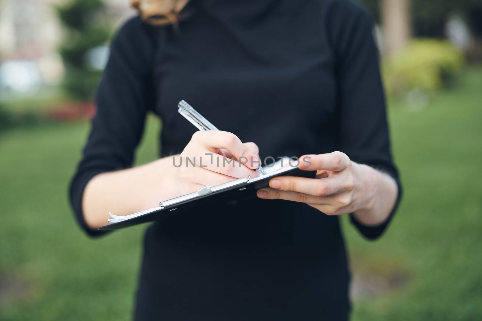 Woman fills out paperwork with pen in hand outdoors cropped view. High quality photo