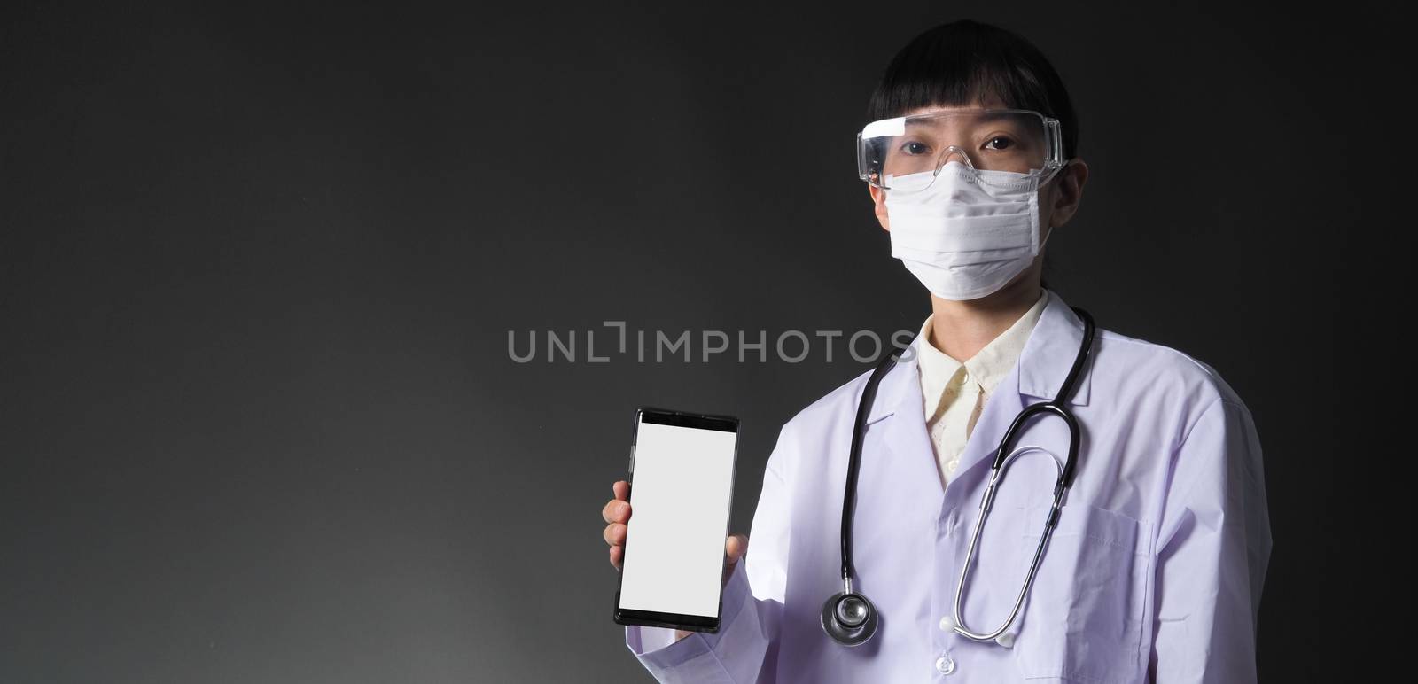 Middle aged of asian woman doctor showing mobile phone screen to communicate something. And she wearing white lab suit, mask and goggle to prevent coronavirus or covid-19