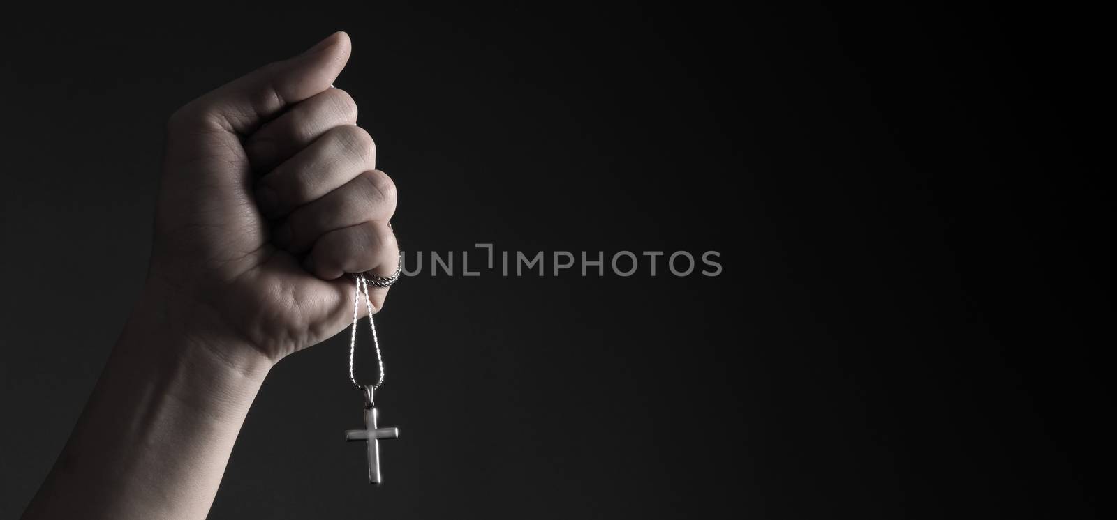 Crucifix pendant or cross sign made from silver and hold in man hand. represent praying for someone that pass away from World pandemic coronavirus and close-up shot black background 