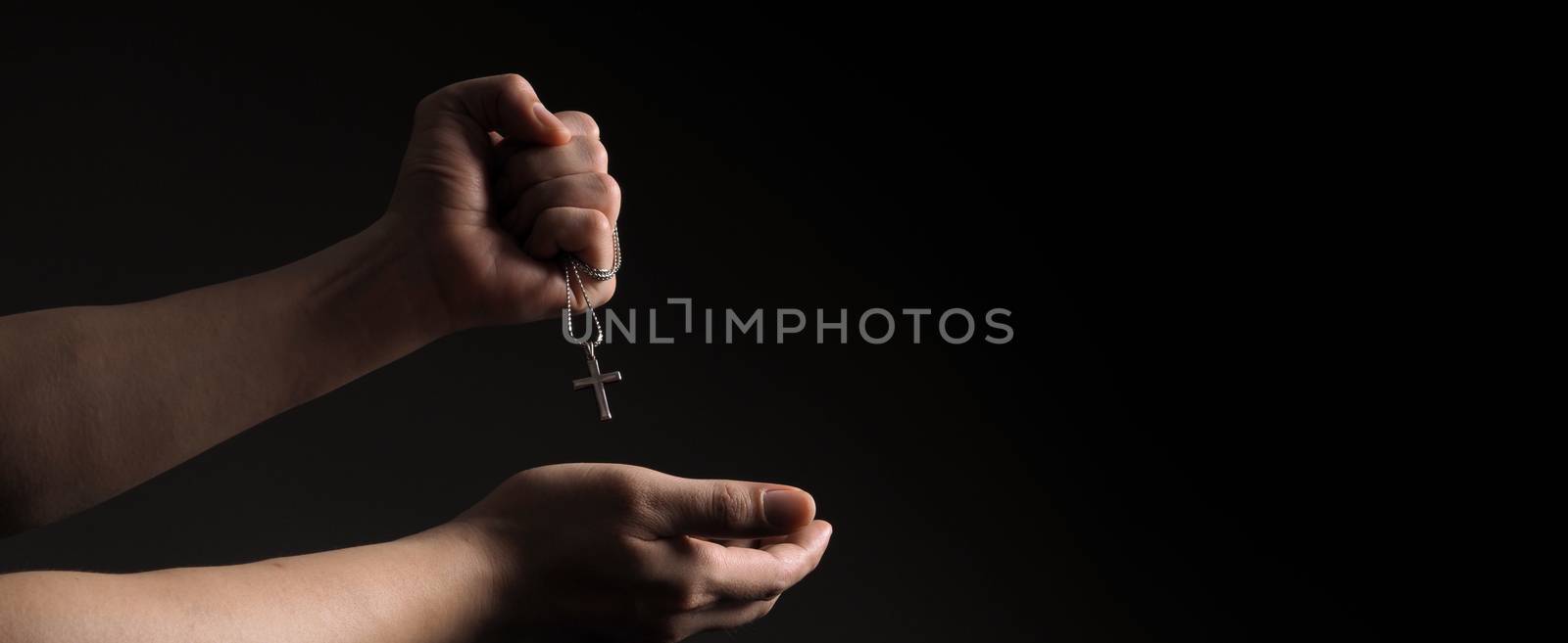 Crucifix pendant or cross sign made from silver and hold in man hand. represent praying for someone that pass away from World pandemic coronavirus and close-up shot black background 