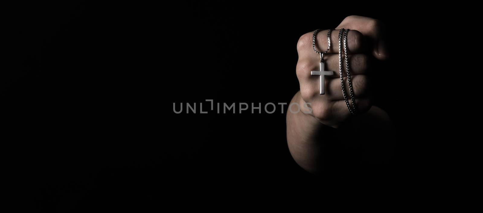 Crucifix pendant or cross sign made from silver and hold in man hand. represent praying for someone that pass away from World pandemic coronavirus and close-up shot black background 