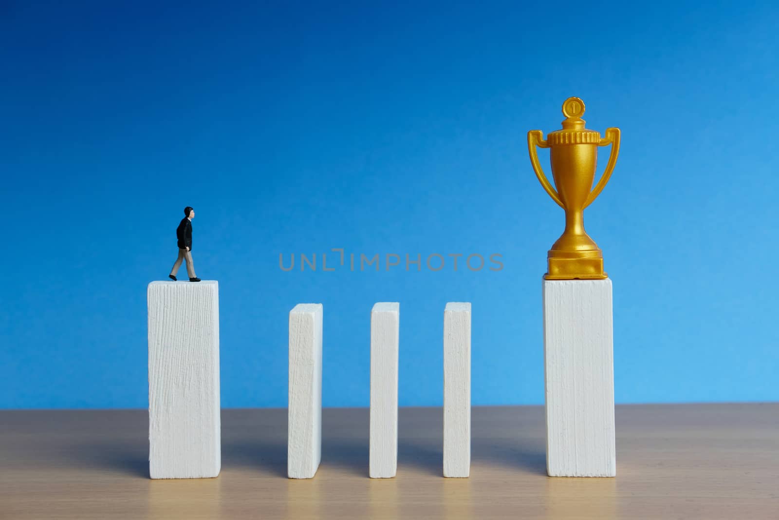 Miniature business concept - businessman walking in stairway obstacle wall to reach golden trophy