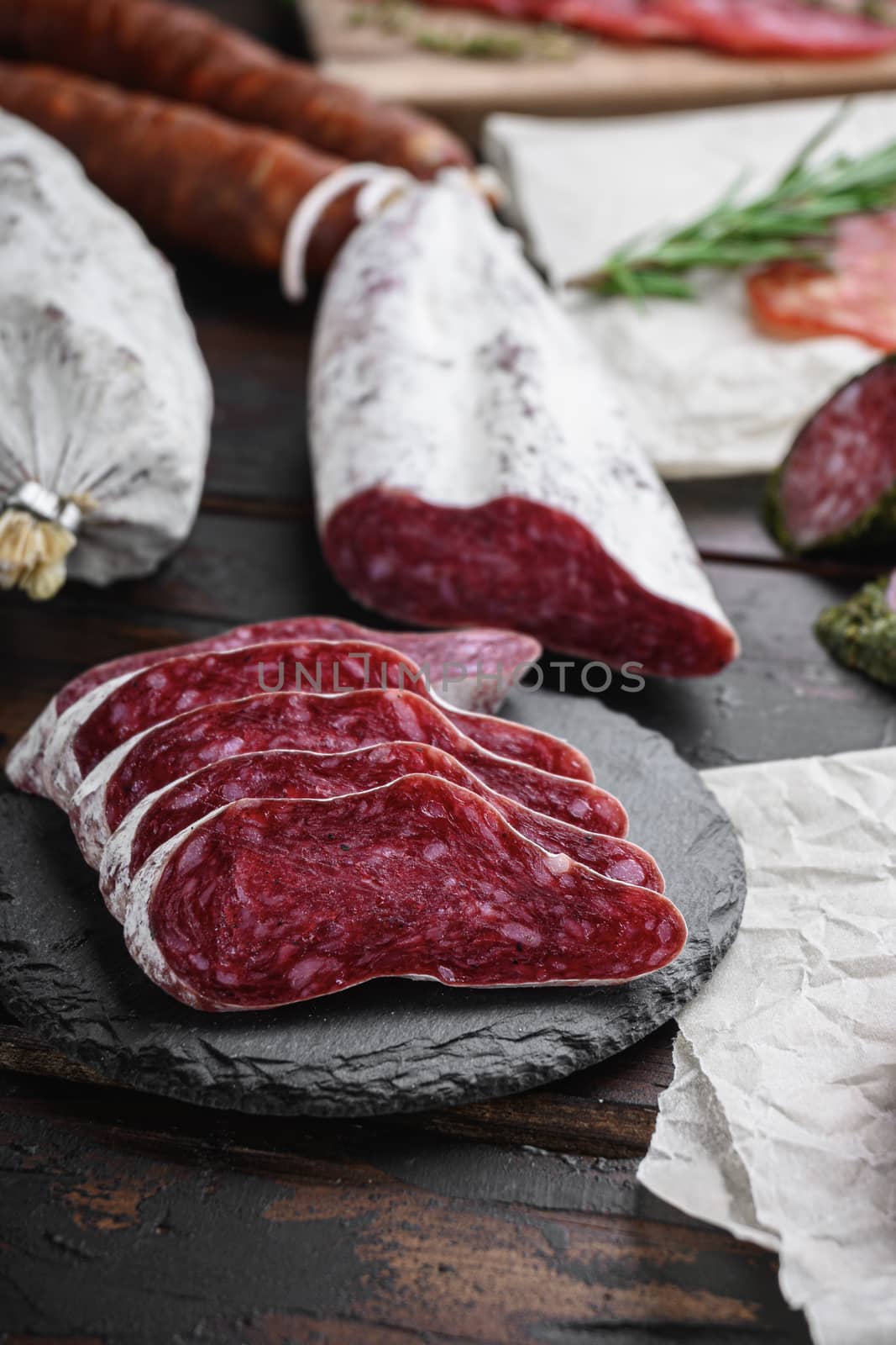 Variety of dry cured chorizo, fuet and other sausages cut in slices with herbs on dark wooden background.