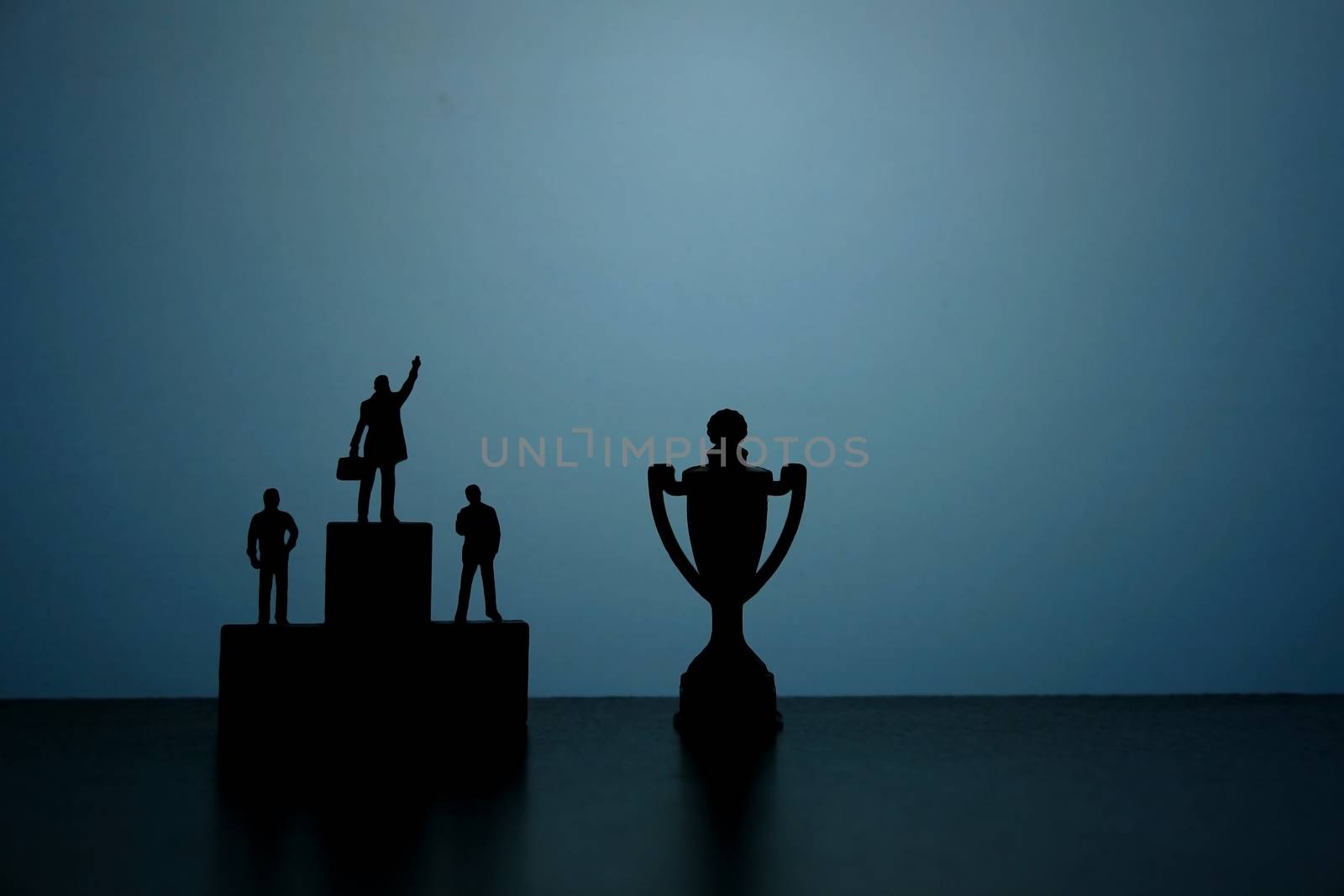 Business strategy conceptual photo - Silhouette of miniature businessman standing on podium while pointing to trophy