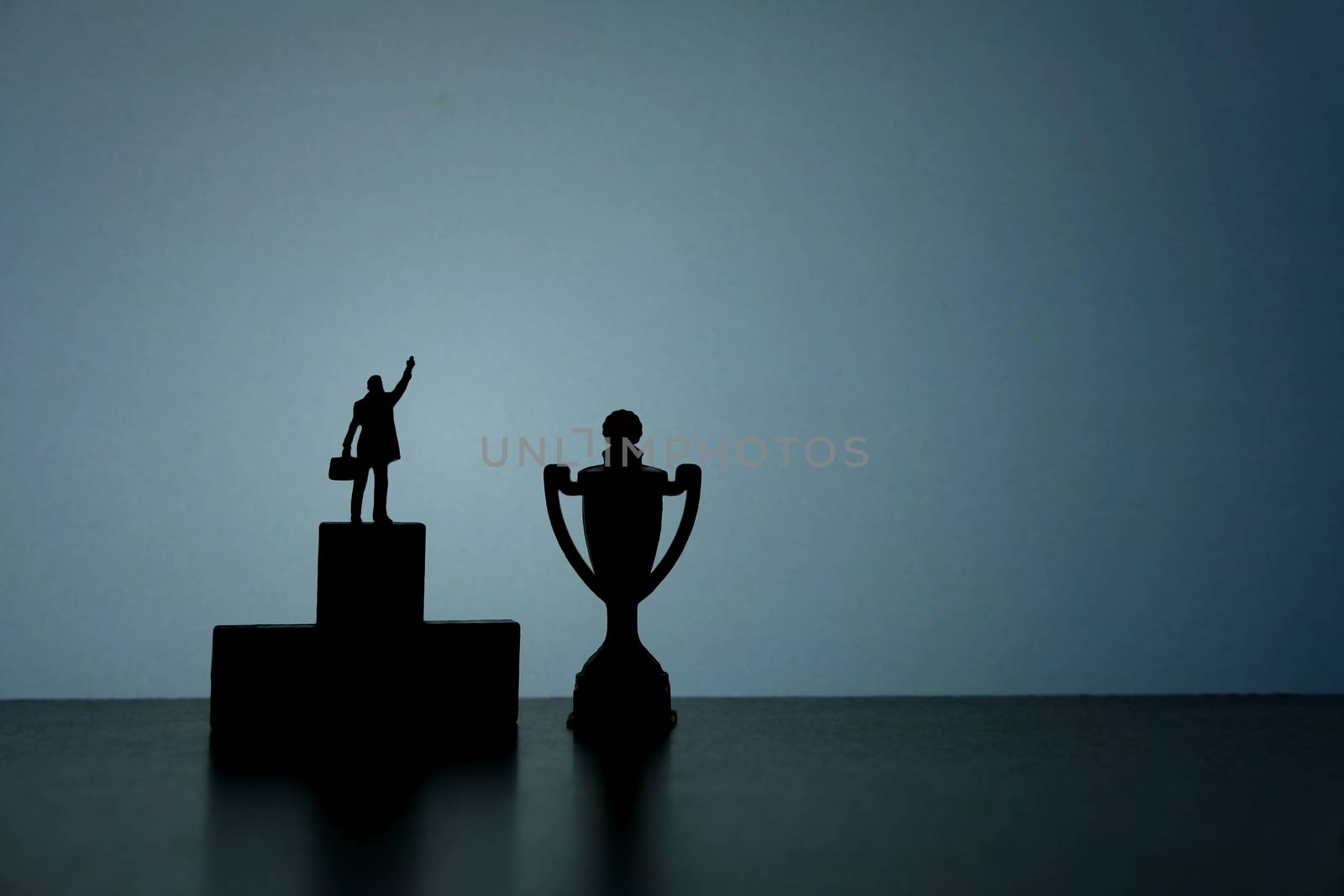 Business strategy conceptual photo - Silhouette of miniature businessman standing on podium pointing on trophy