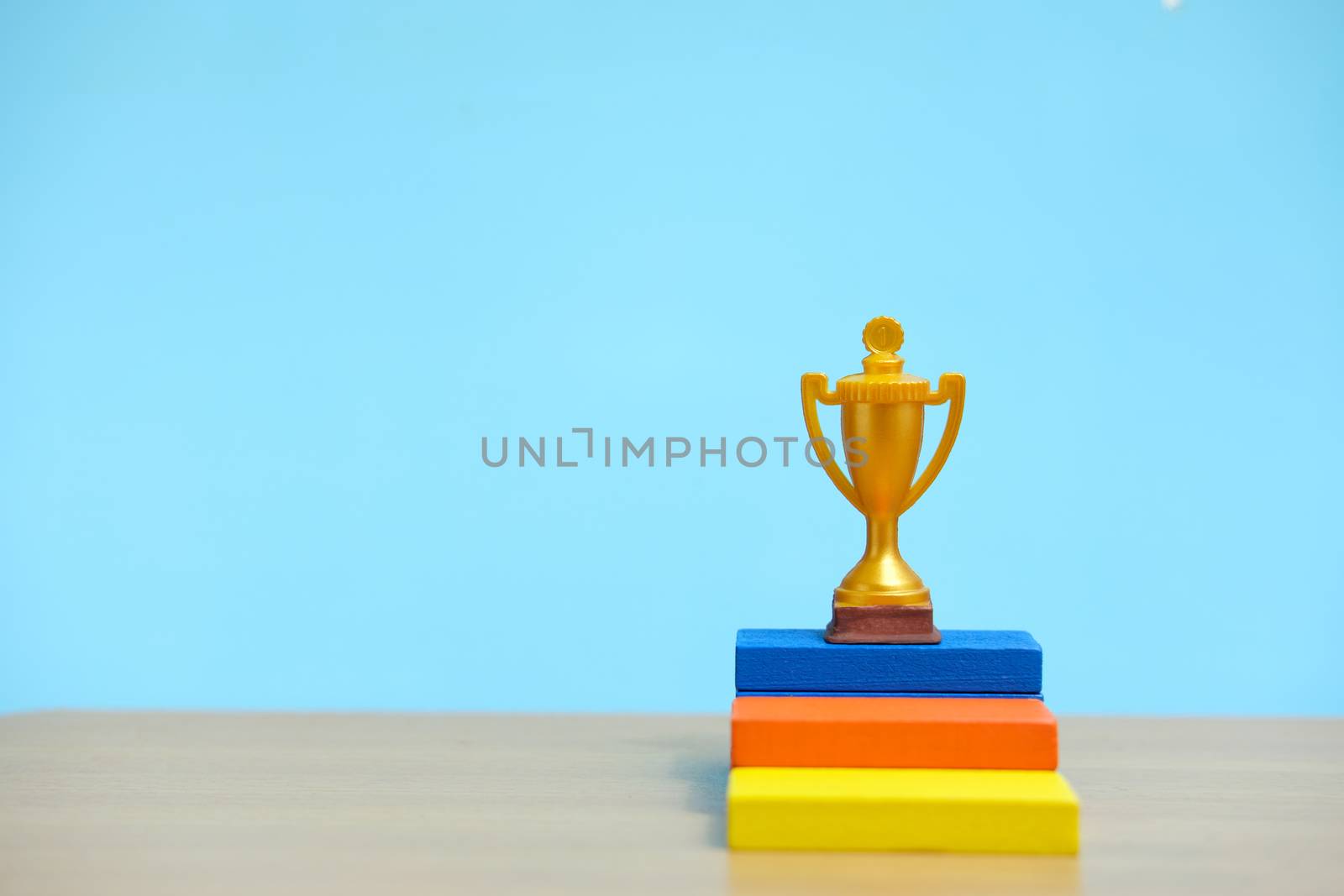 Golden trophy standing at colorful podium on wooden table