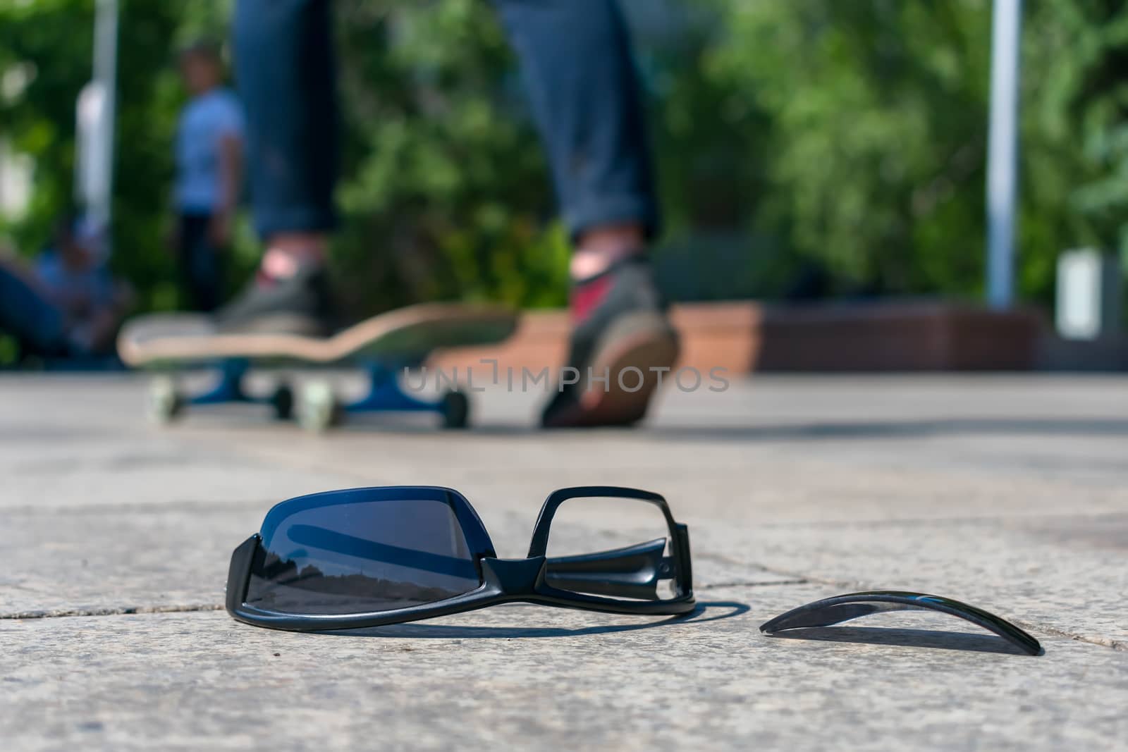 Skateboarder dropped his black glasses on the asphalt while riding the board