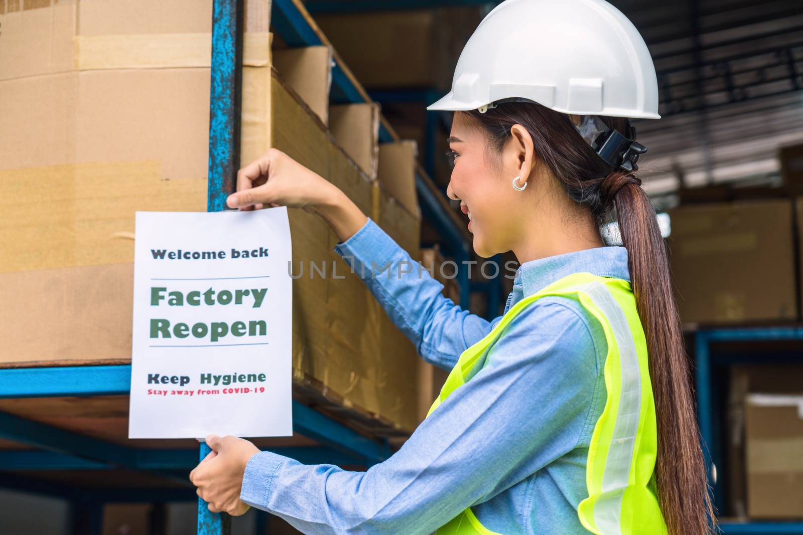 Asian woman worker with safety clothes putting the Factory reopen notice paper for welcome back to customer into local warehouse again after covid19 outbreak, business and export  industry concept