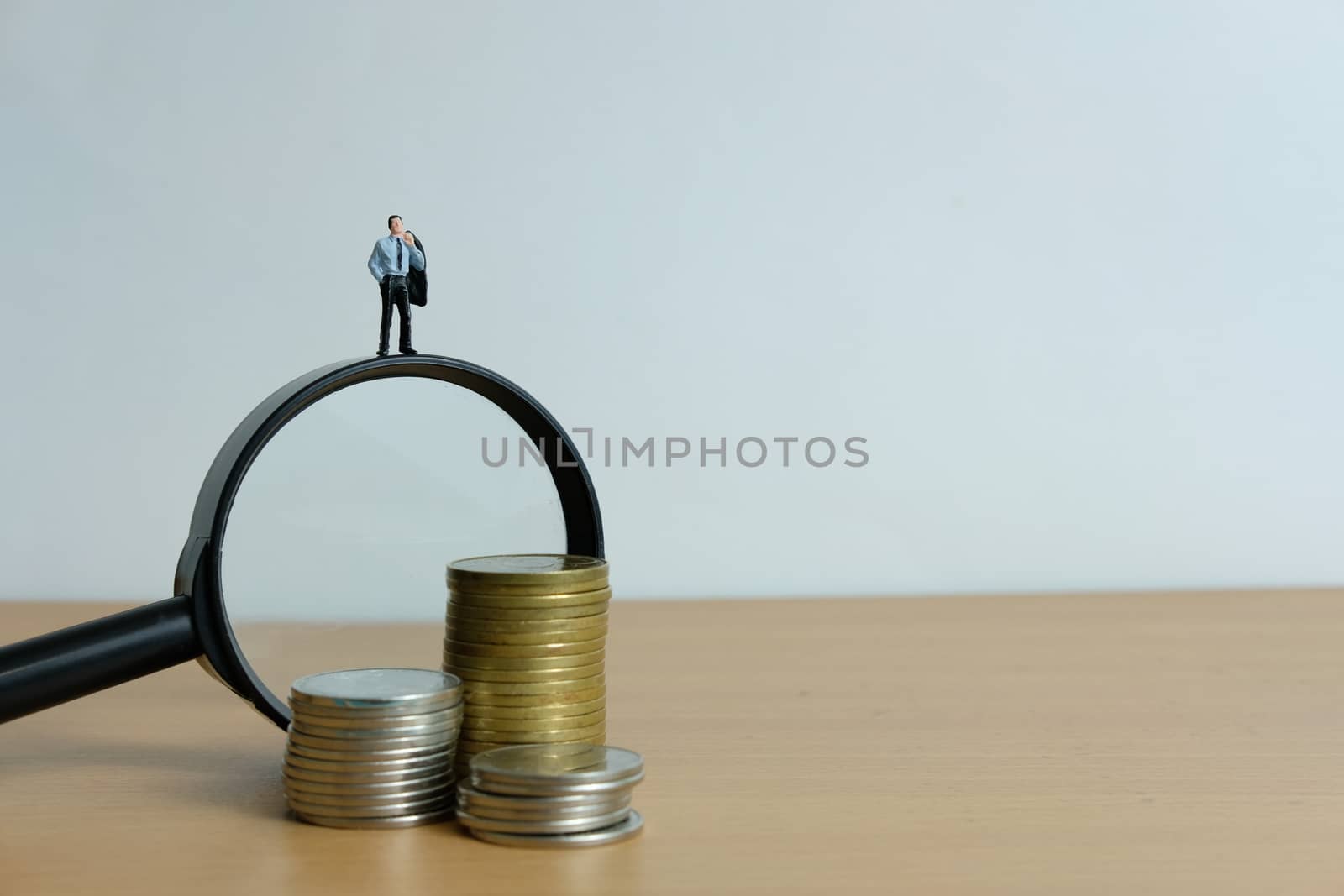 Miniature people concept - a businessman standing on magnifier glass, searching for financial solution