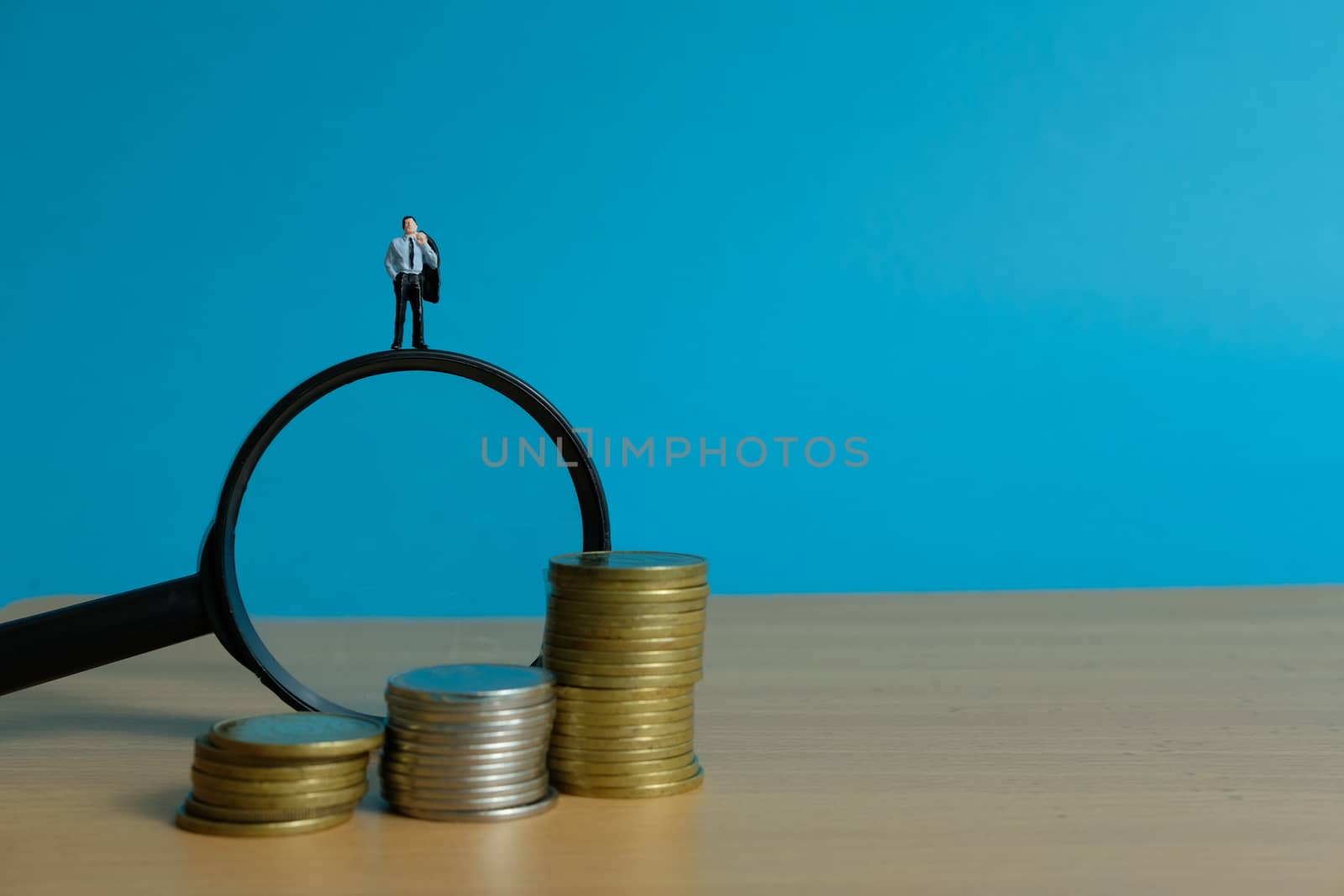 Miniature people concept - a businessman standing on magnifier glass, searching for financial solution