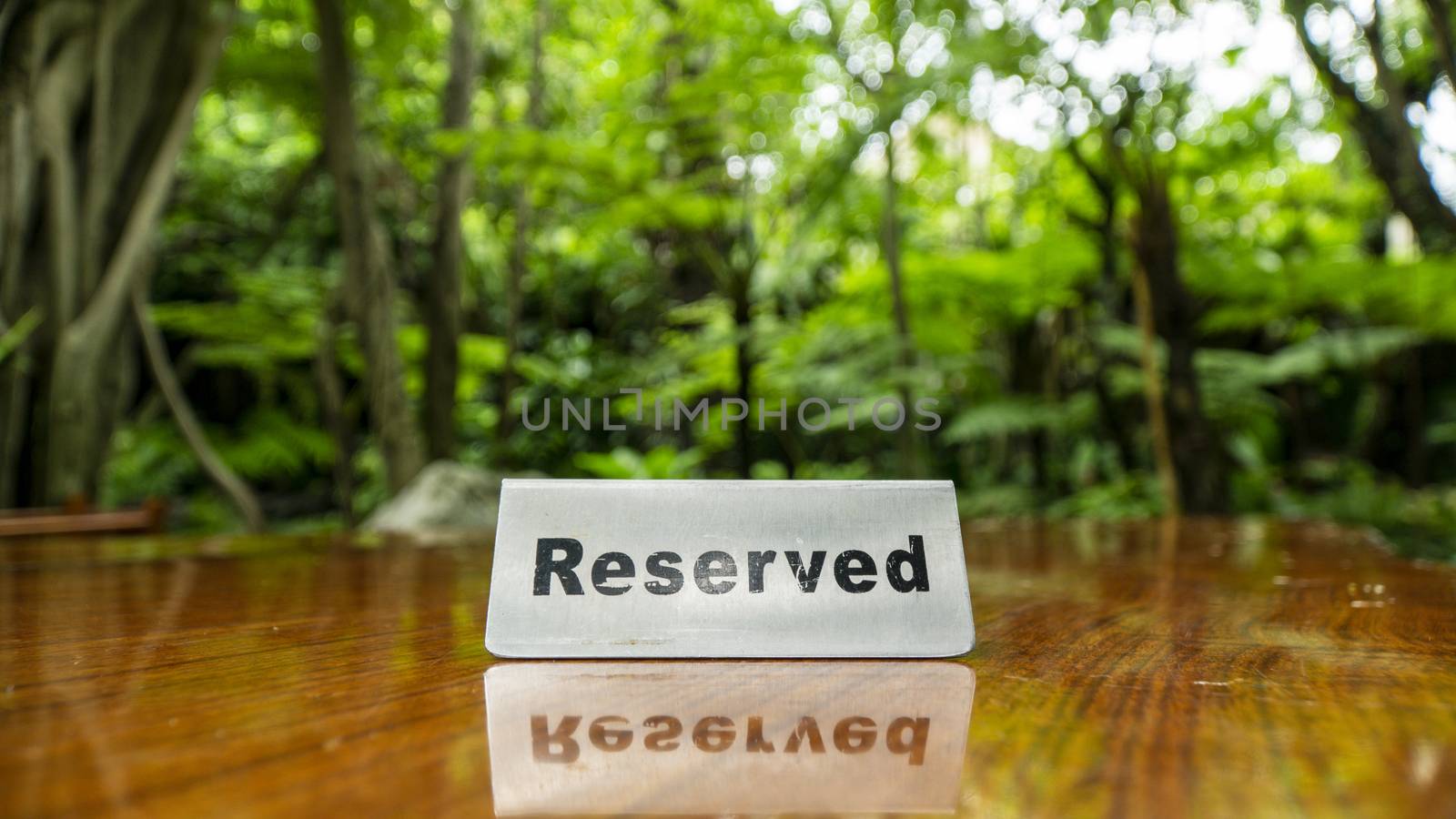 Reserved sign made out stainless steel plate on a laminated wooden table of a restaurant with trees and forest in the background.