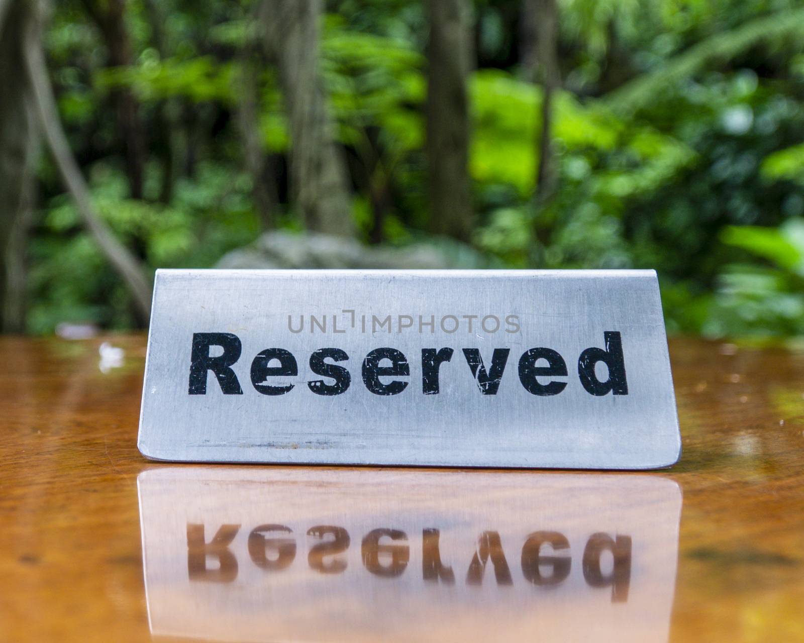 Reserved sign made out stainless steel plate on a laminated wooden table of a restaurant with trees and forest in the background. by sonandonures