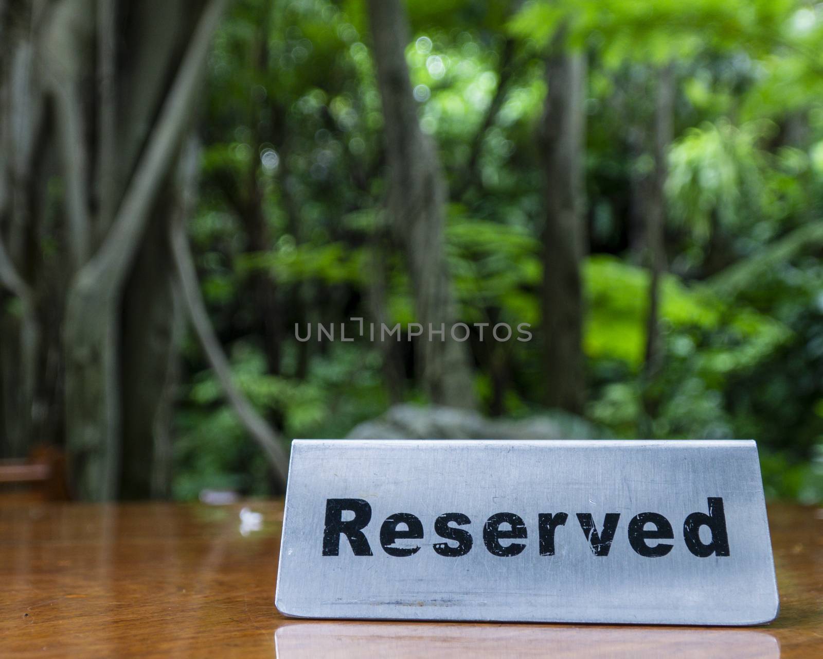 Reserved sign made out stainless steel plate on a laminated wooden table of a restaurant with trees and forest in the background.