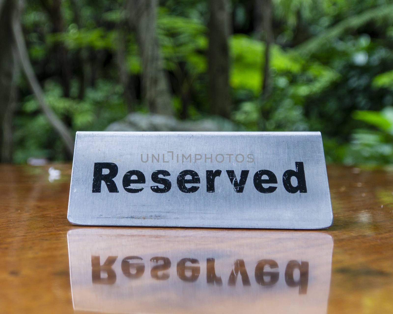 Reserved sign made out stainless steel plate on a laminated wooden table of a restaurant with trees and forest in the background.