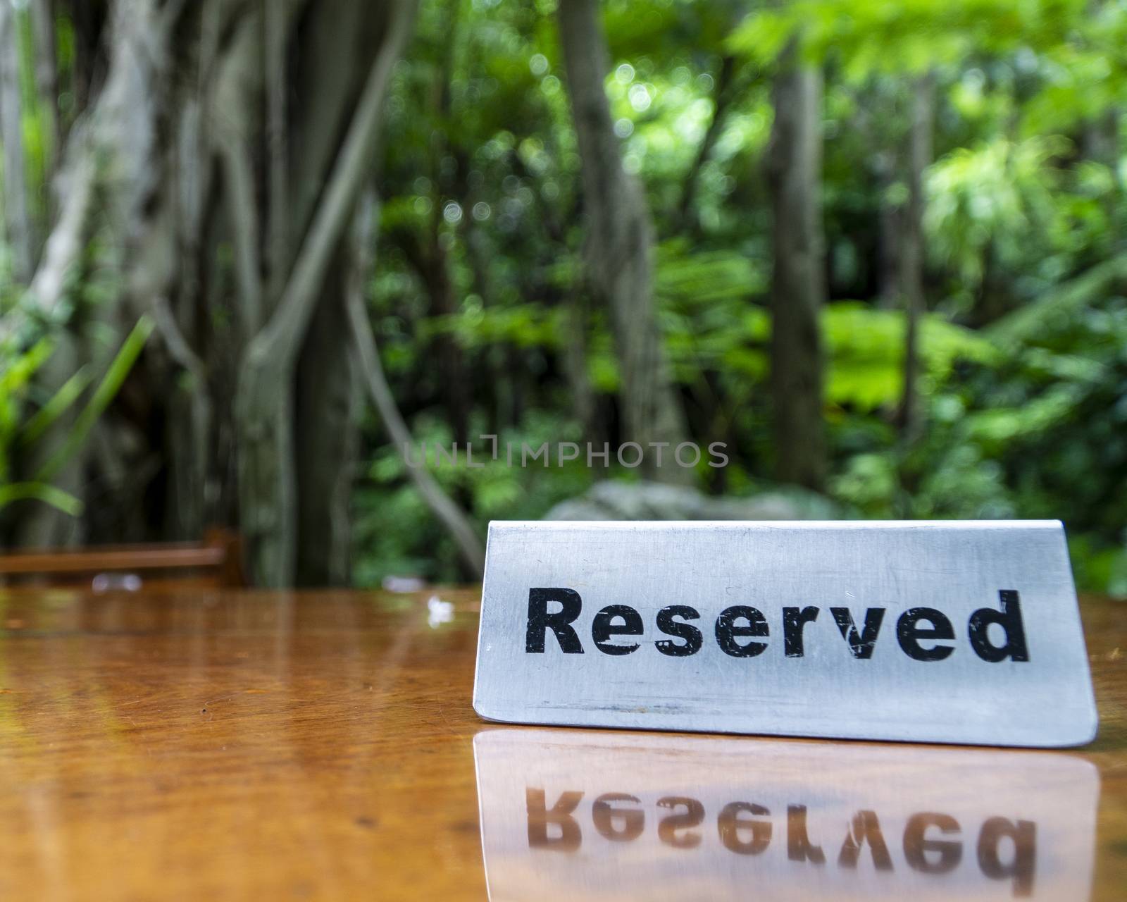 Reserved sign made out stainless steel plate on a laminated wooden table of a restaurant with trees and forest in the background.