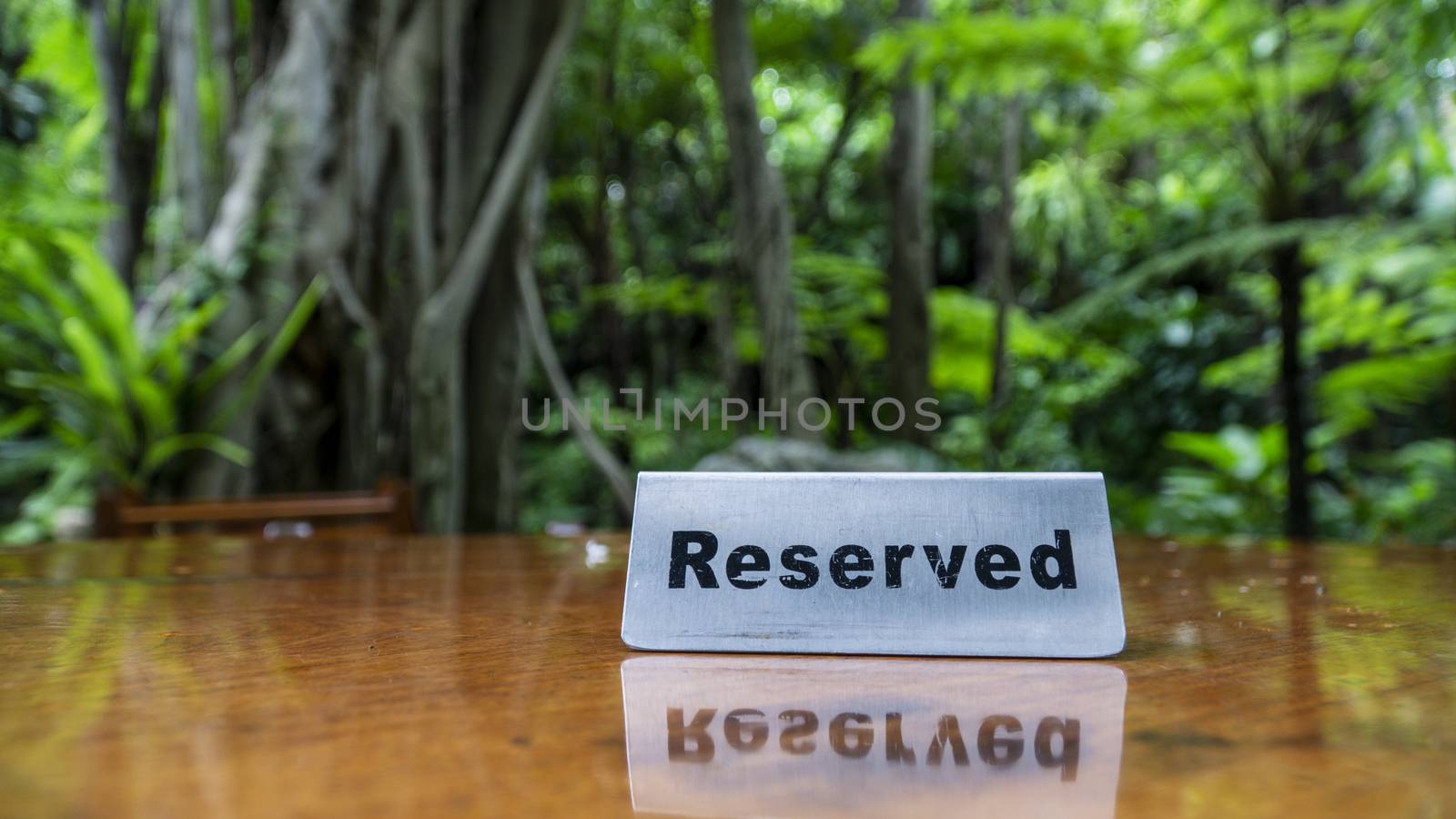 Reserved sign made out stainless steel plate on a laminated wooden table of a restaurant with trees and forest in the background.