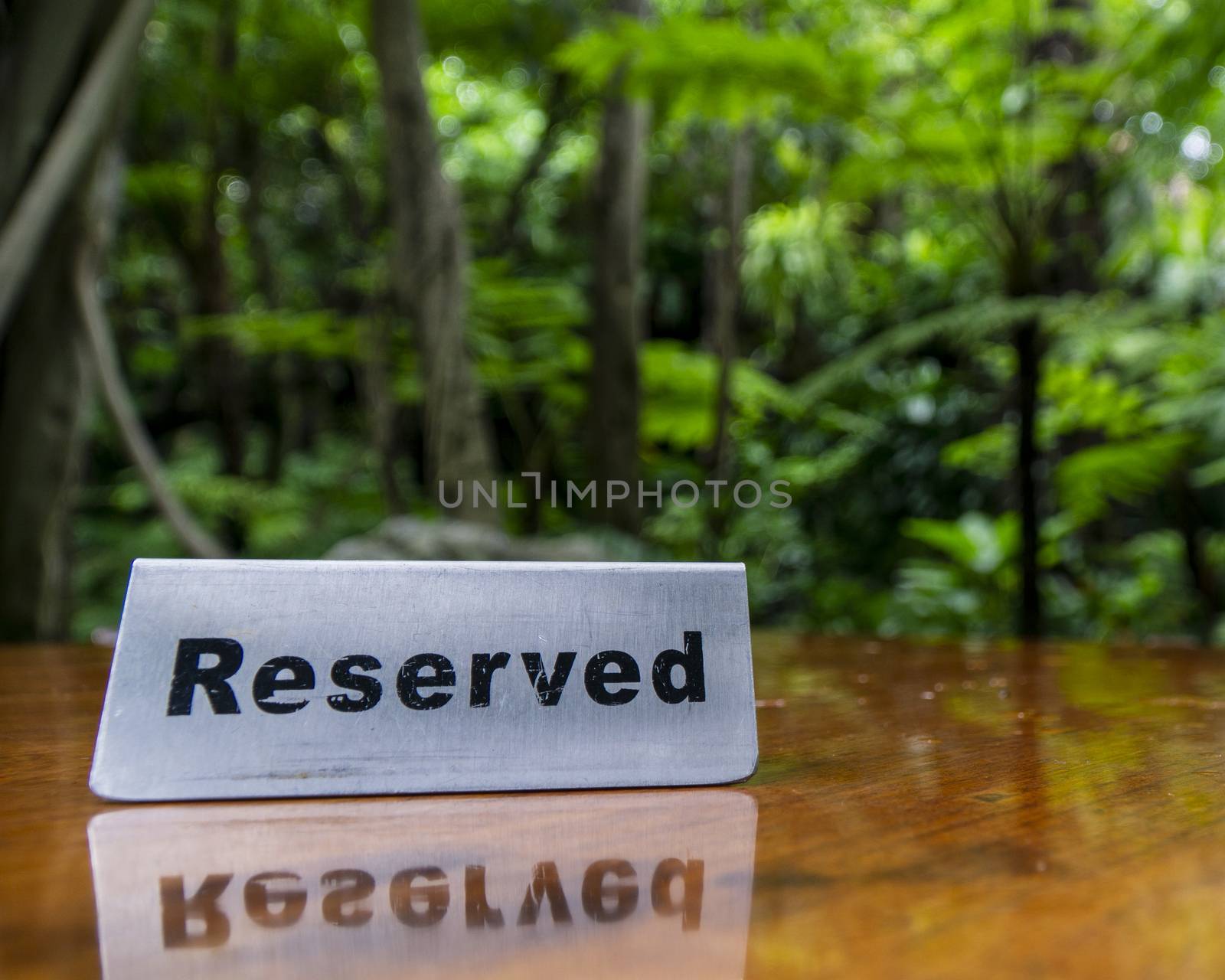 Reserved sign made out stainless steel plate on a laminated wooden table of a restaurant with trees and forest in the background.