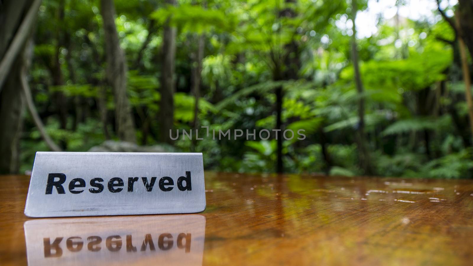 Reserved sign made out stainless steel plate on a laminated wooden table of a restaurant with trees and forest in the background. by sonandonures