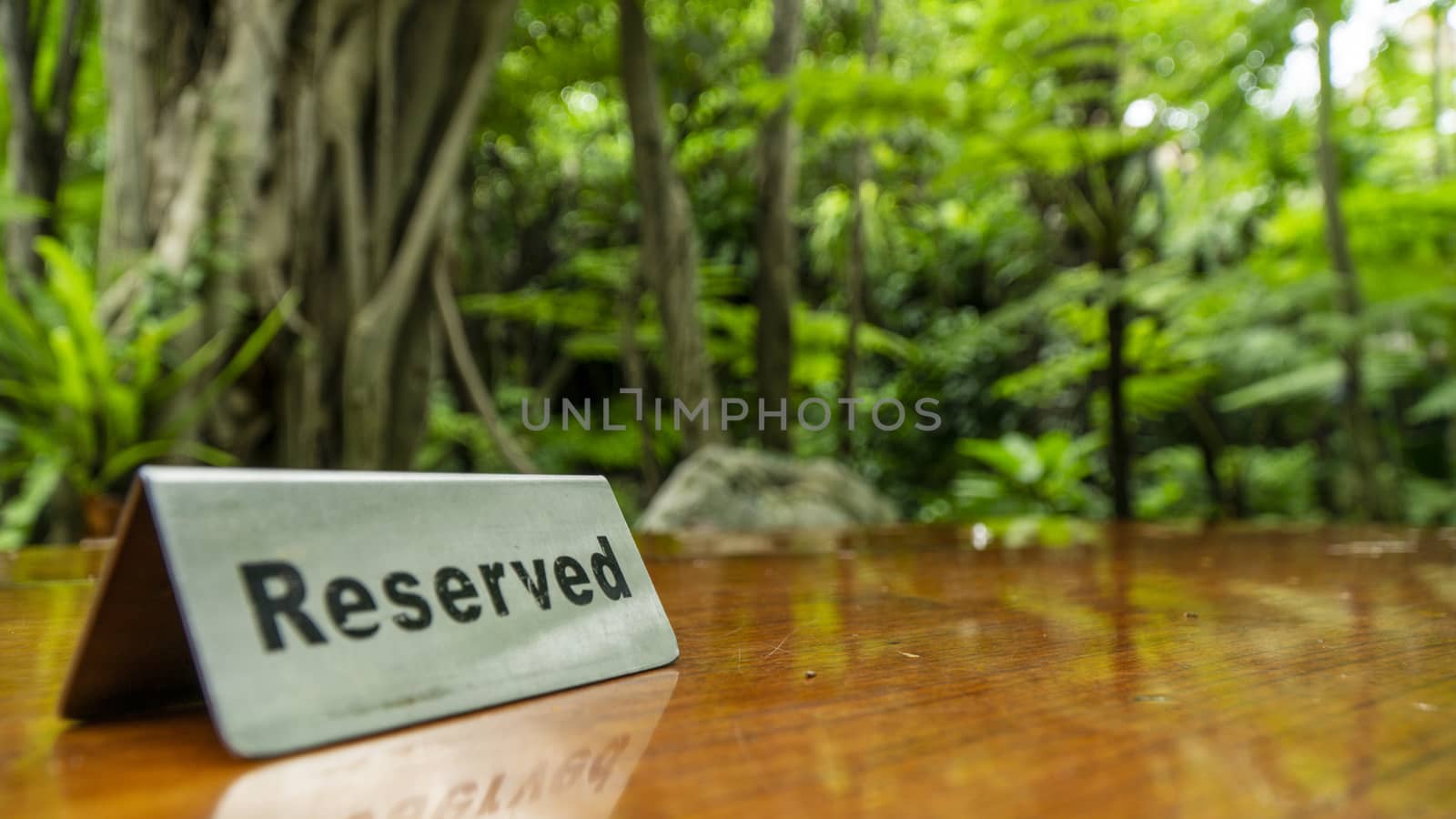 Reserved sign made out stainless steel plate on a laminated wooden table of a restaurant with trees and forest in the background.