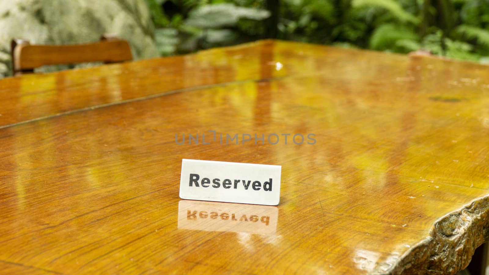 Reserved sign made out stainless steel plate on a laminated wooden table of a restaurant with trees and forest in the background. by sonandonures