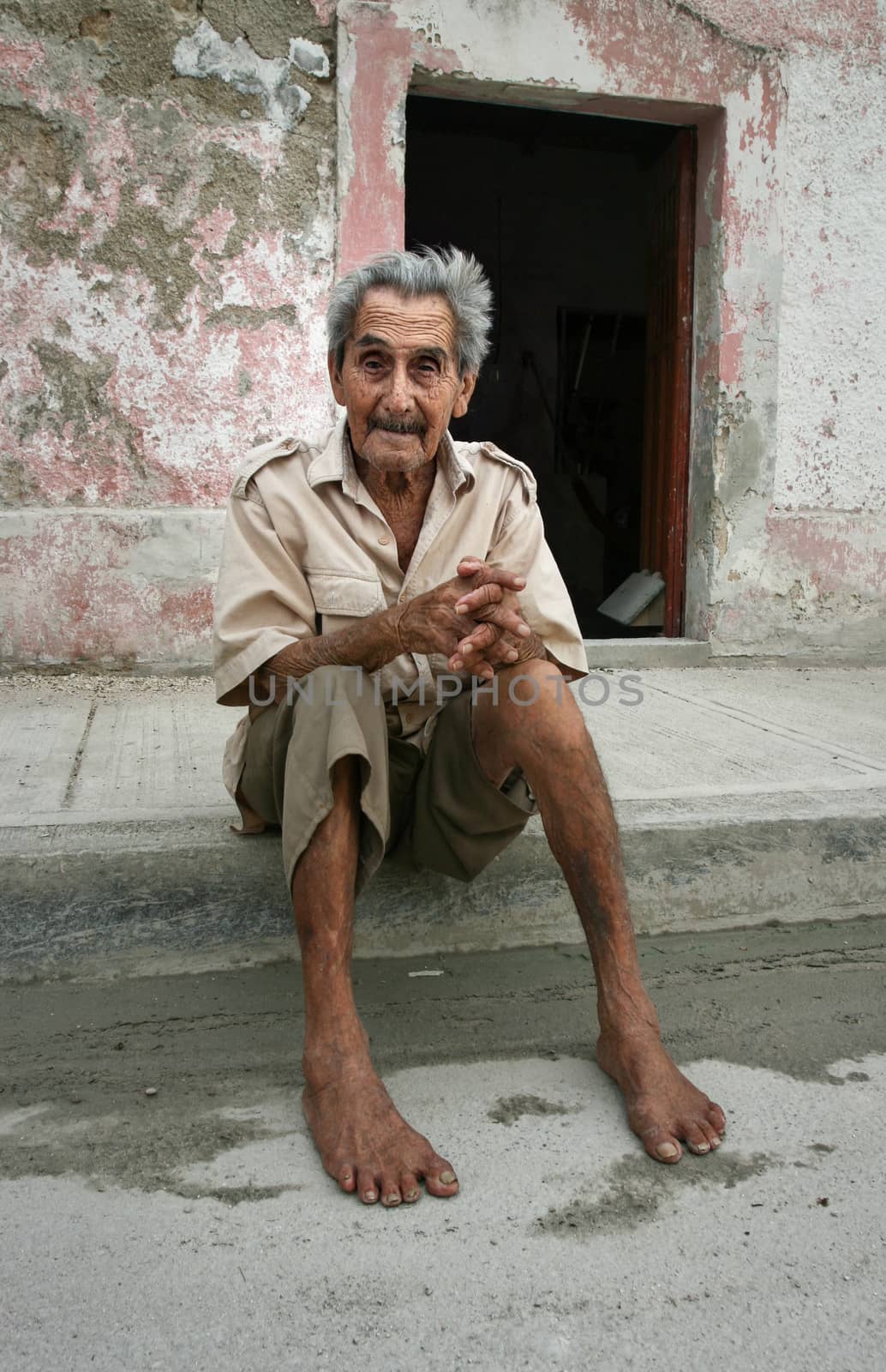 Celestun, Mexico - October 9, 2007: Poor Celestun resident sitting barefoot on his porch ground on a hot day with tired expression in his face.