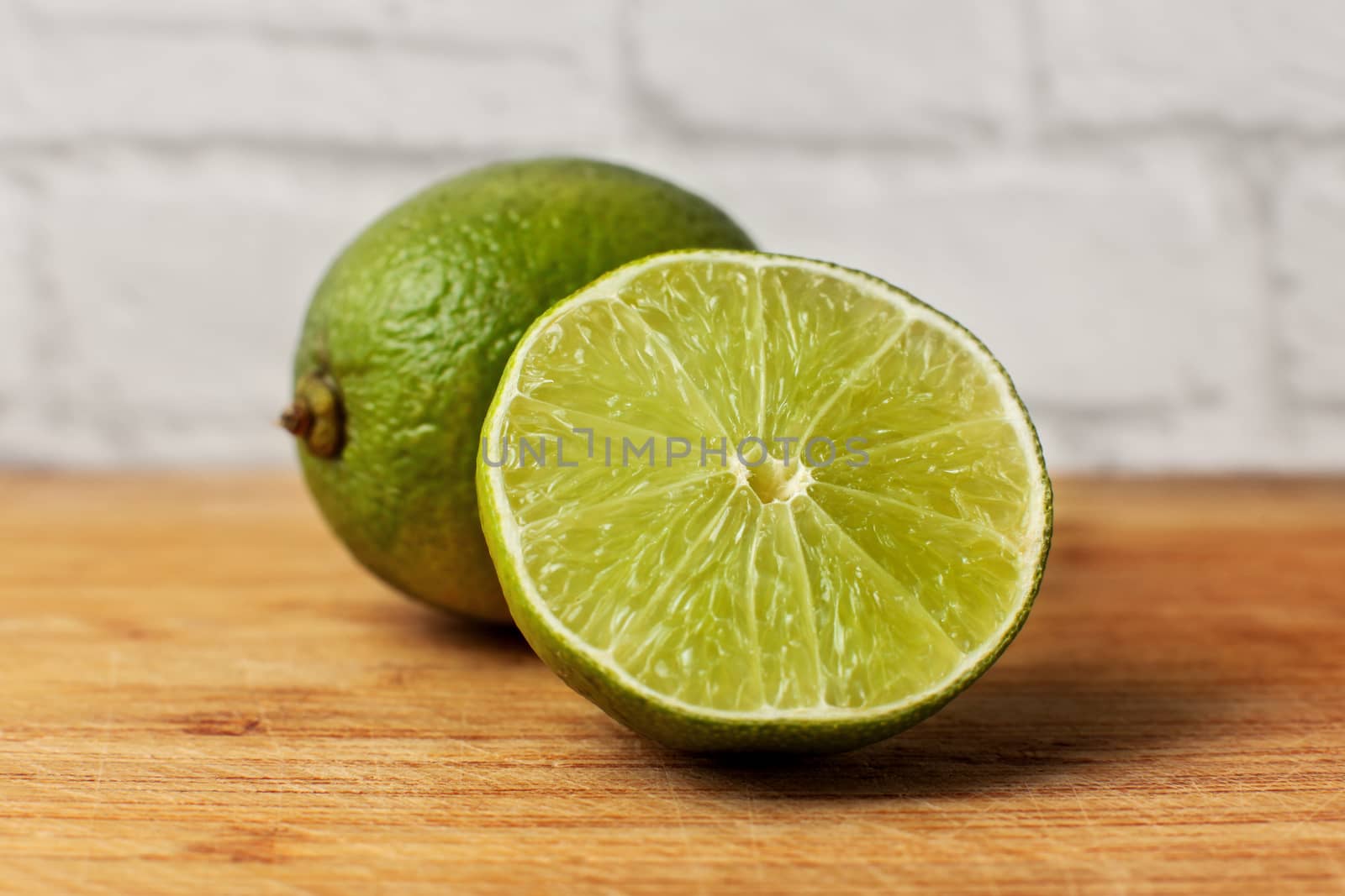 Whole lime and other one cut in half, on an old wooden cutting board.