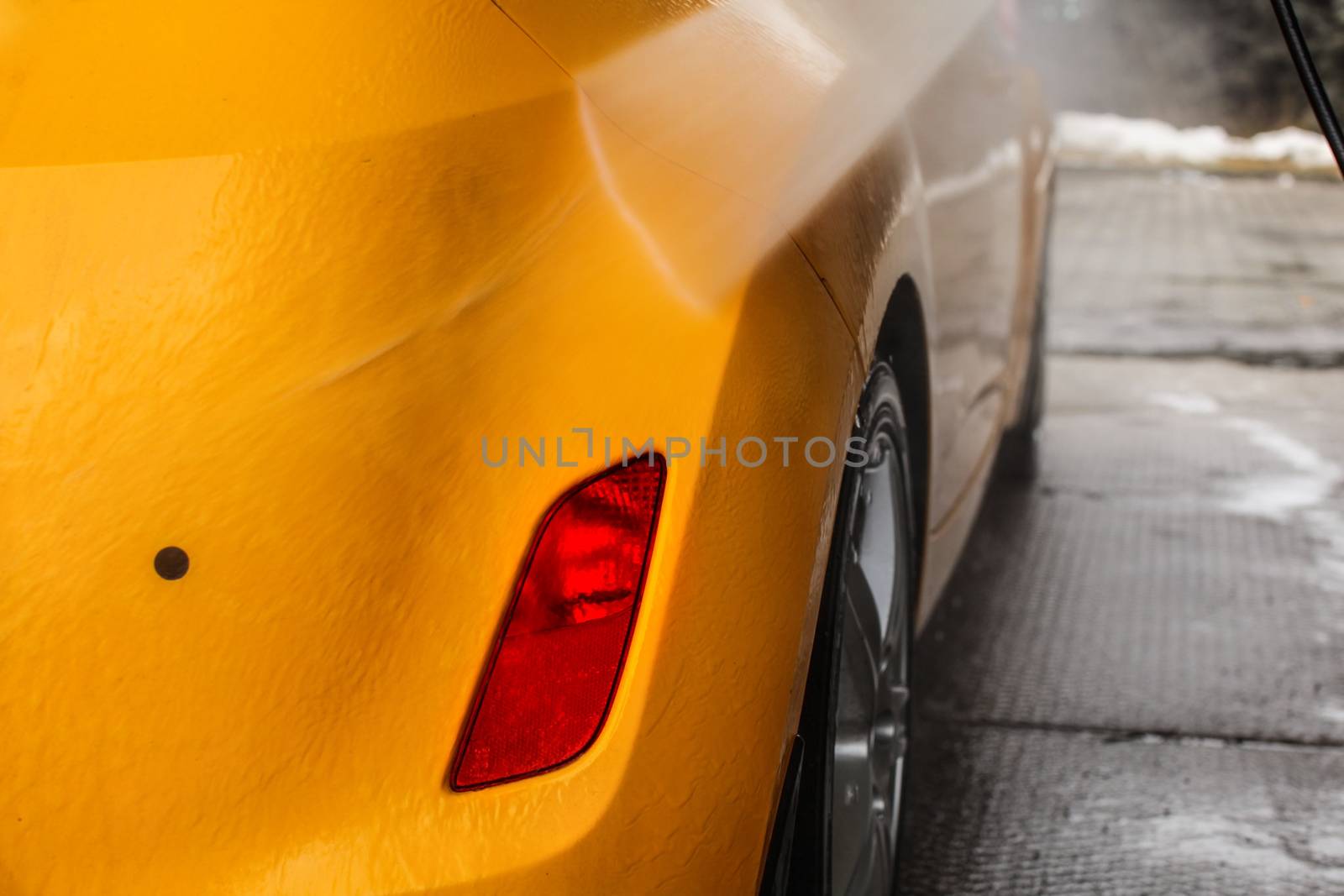 Detail on dark yellow car back being washed with jet water stream in carwash.