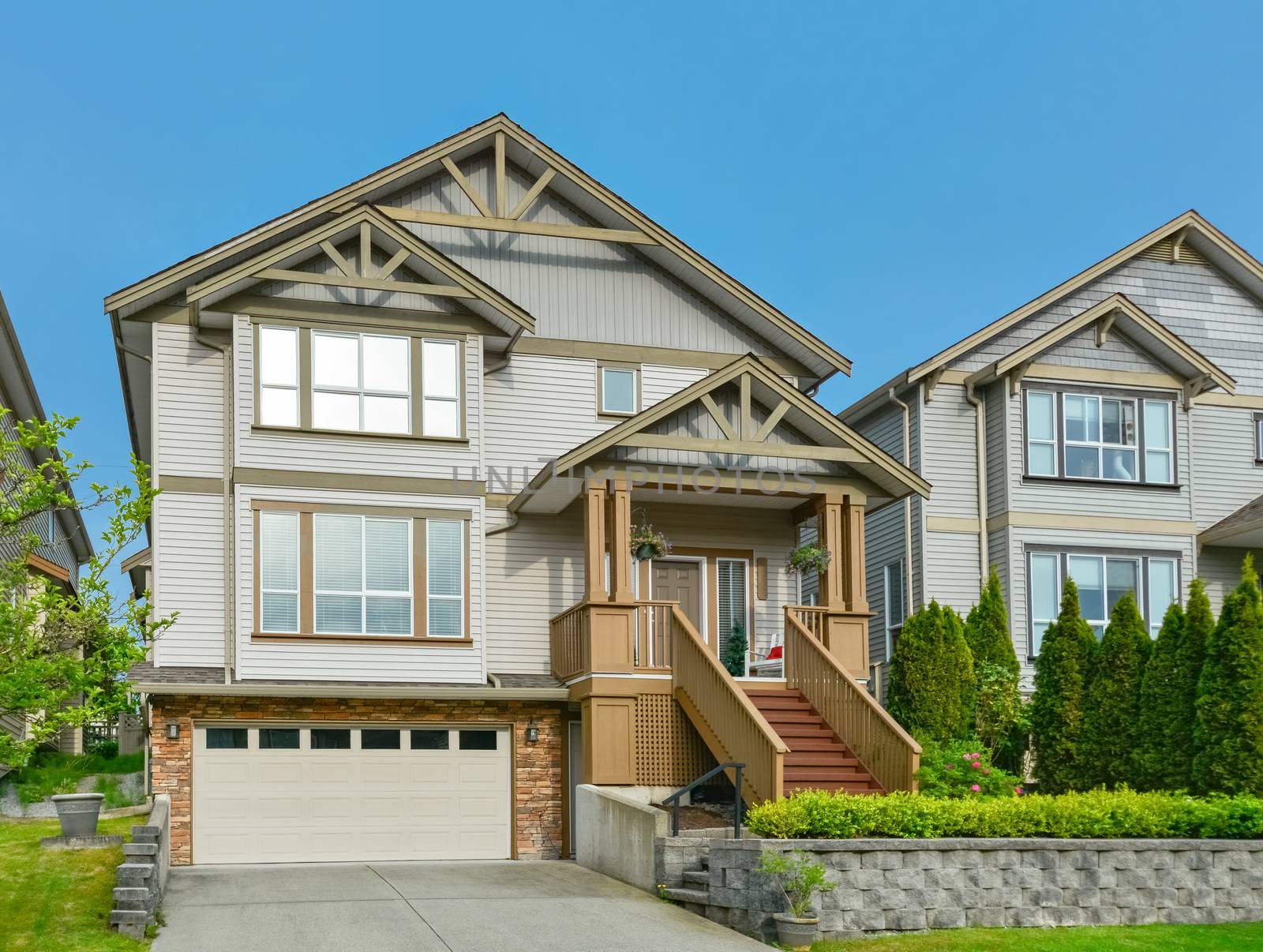 Main entrance of residential house with concrete driveway and small front yard on land terrace. 3 levels family house with porch and doorsteps