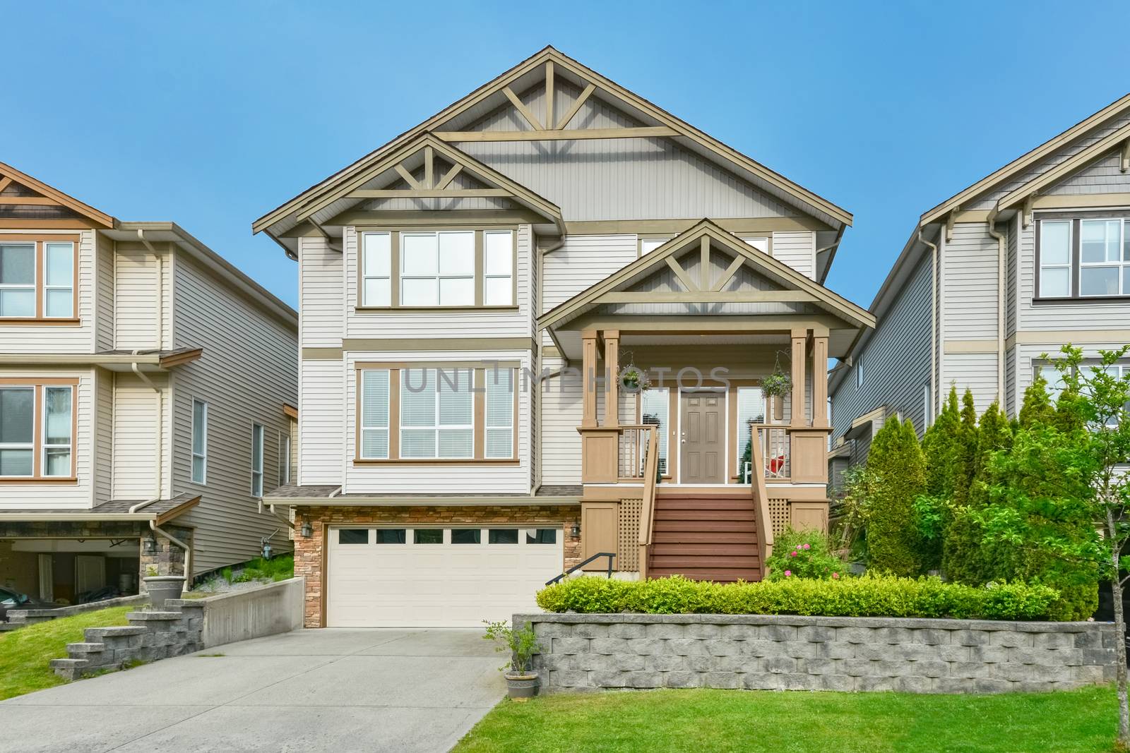 Main entrance of residential house with concrete driveway and small front yard on land terrace. 3 levels family house with porch and doorsteps
