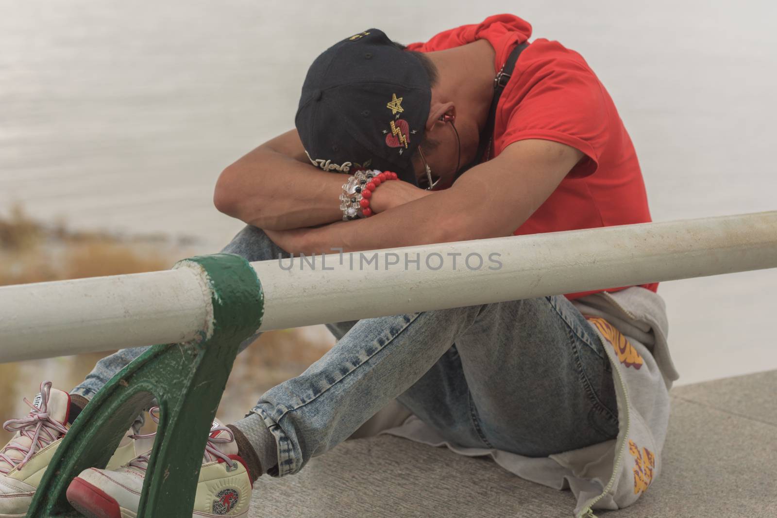 Harbin, Heilongjiang, China - September 2018: Young boy sitting alone with sad feeling. Guy sitting on the bridge