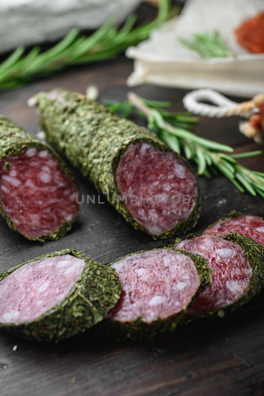 Variety of dry cured chorizo, fuet and other sausages cut in slices with herbs on dark wooden background.
