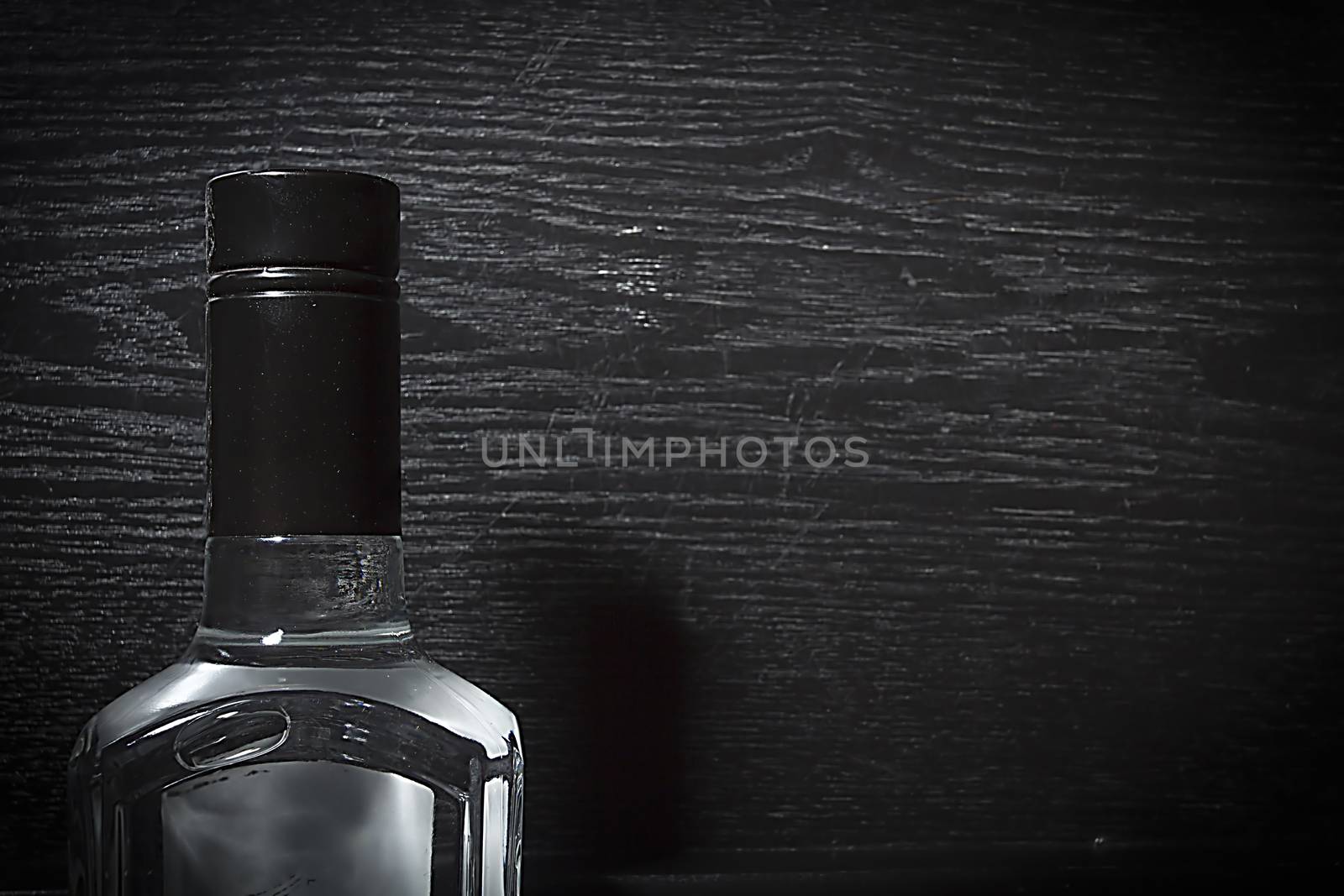 Neck of bottle with vodka on black wooden background