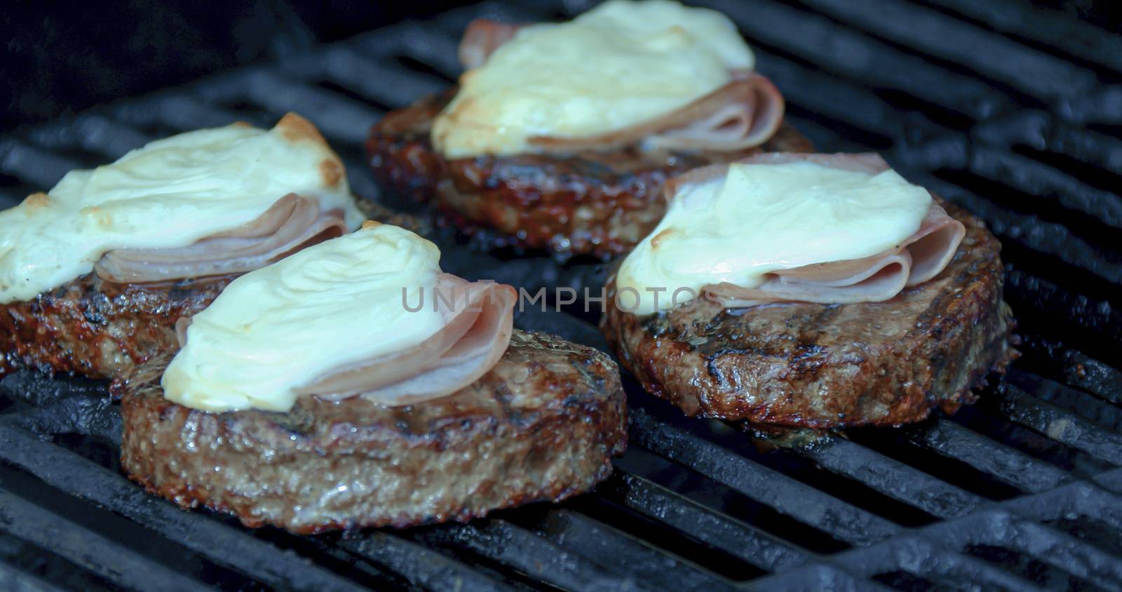 Cooking a burger patty with melted cheese and ham on a grill by oasisamuel
