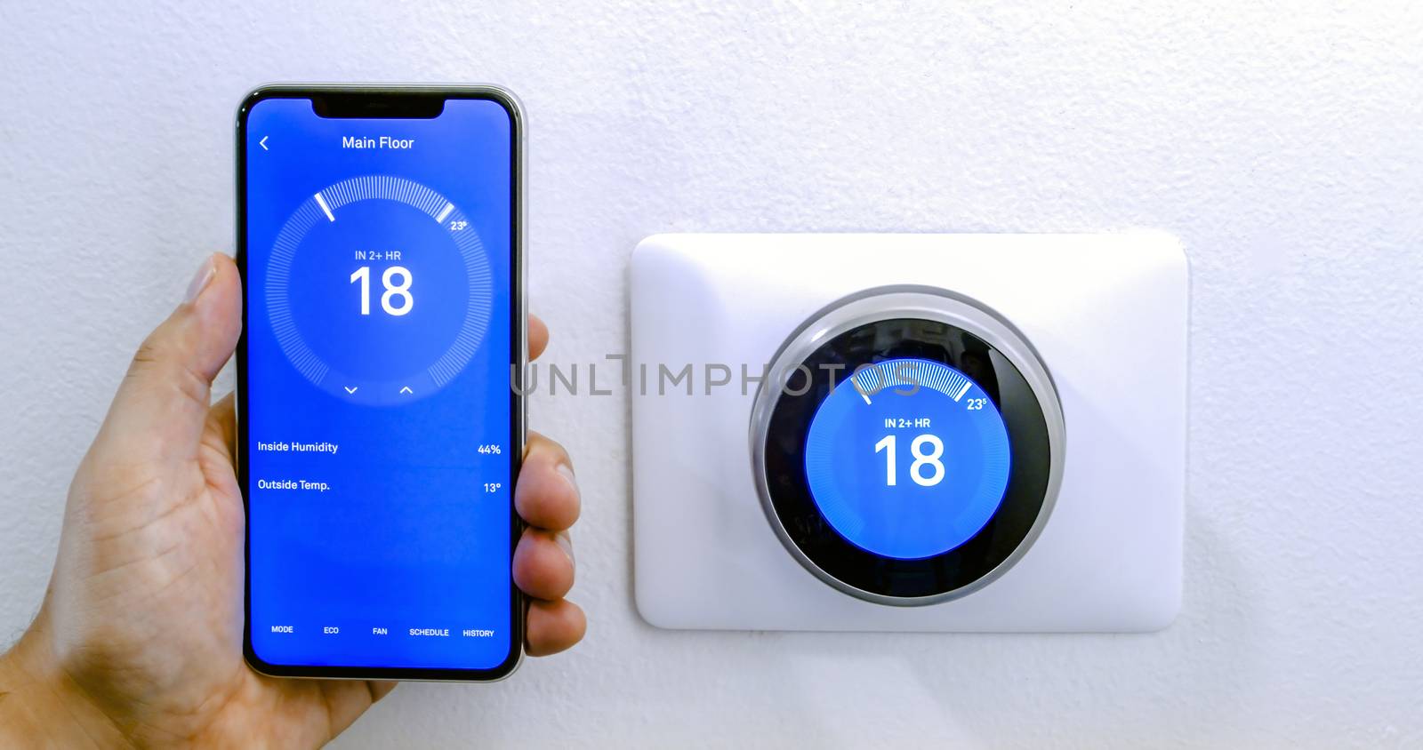 Calgary, Alberta, Canada. Aug. 29, 2020. A person cooling down with air conditioner with a iPhone 11 Pro Max using the nest app on celsius metrics using a wireless Nest Learning Thermostat on a white wall.