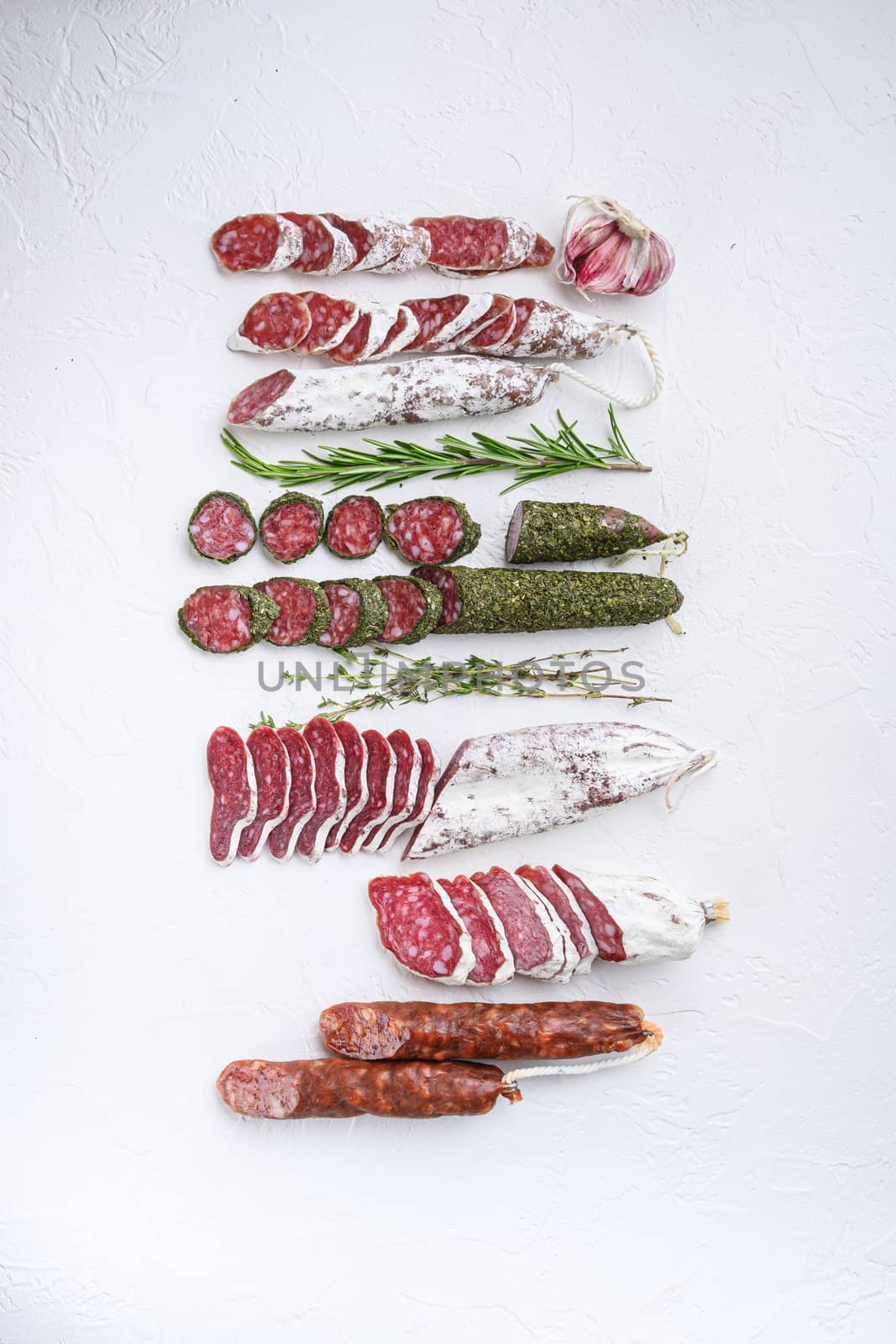 Variety of dry cured fuet and chorizosalami sausages, whole and sliced on white surface, top view.