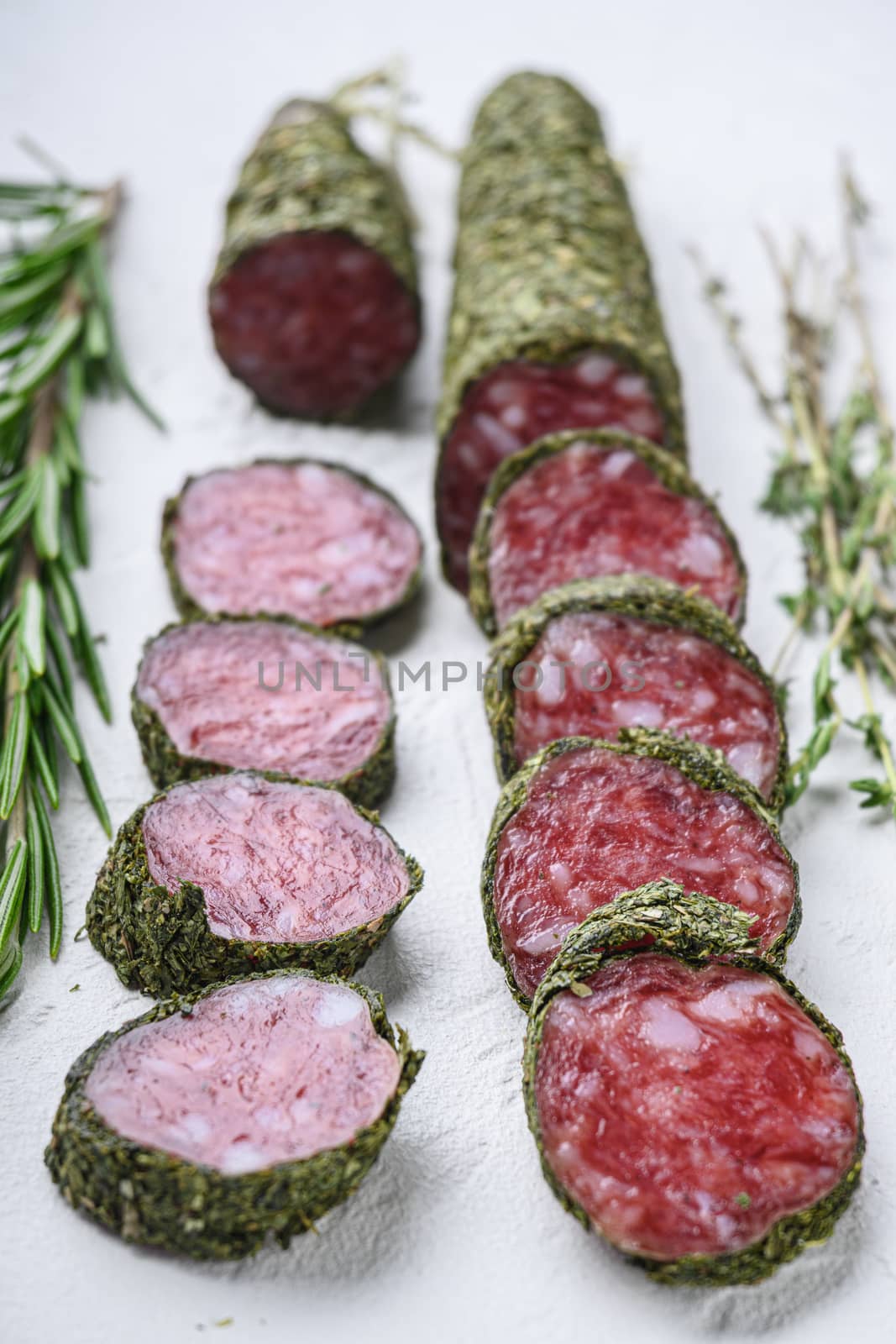 Variety of dry cured fuet and chorizosalami sausages, whole and sliced on white surface.