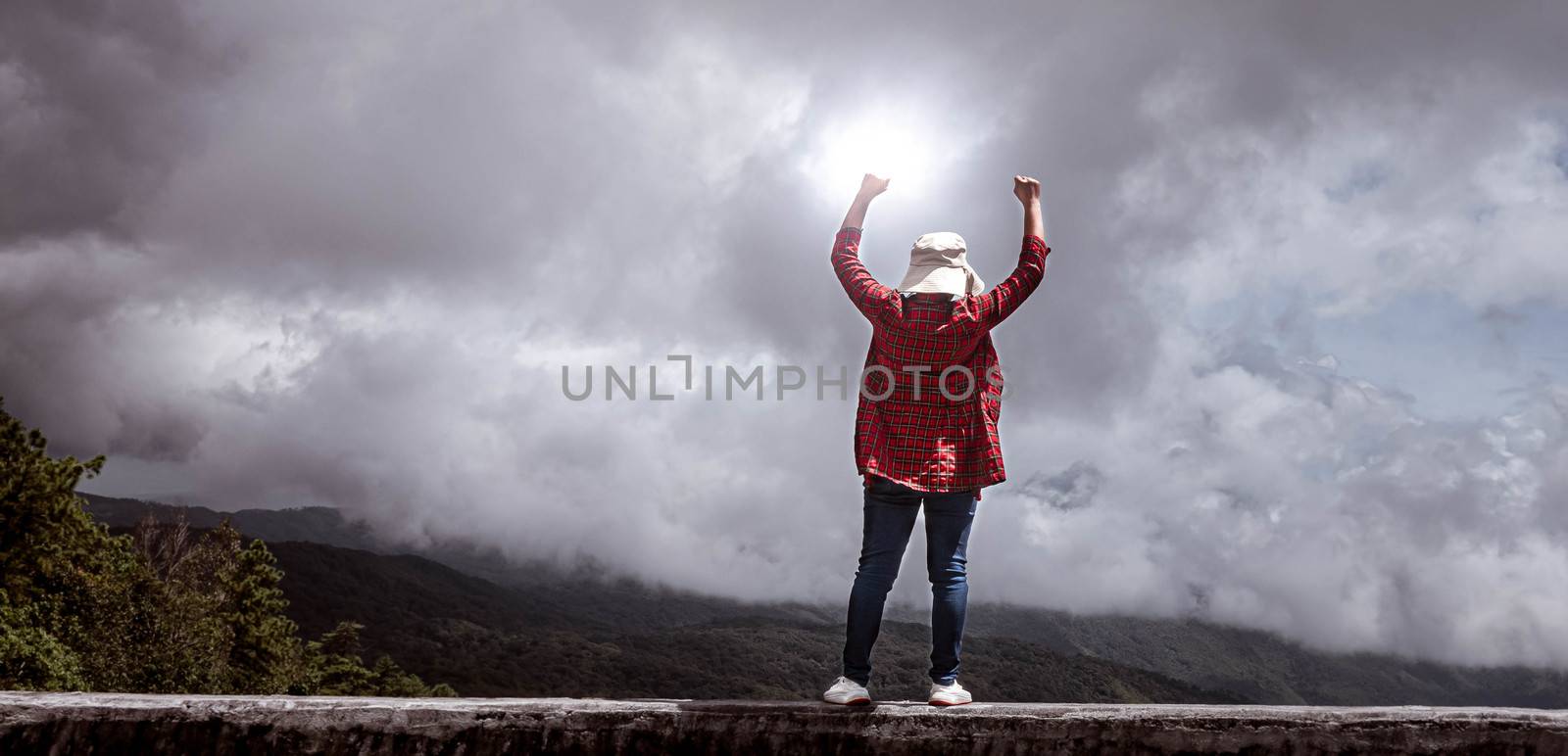 Female standing with success with fists raised up on peak of mountain with sky background.  Achievement and winning concept.